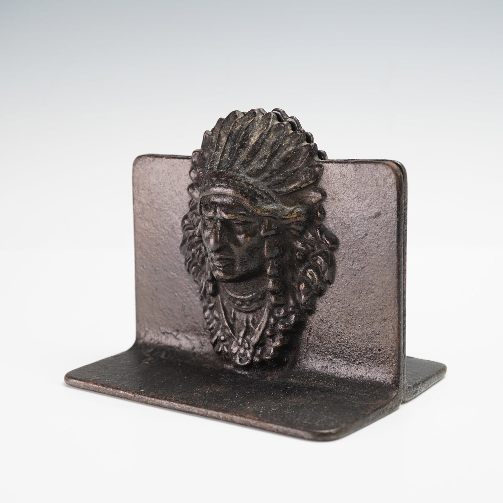 Pair of Metal Bookends, Indian Chief: A pair of cast metal bookends, each featuring a relief of an Indian chief wearing a feathered headdress. Finished in a dark bronze tone with natural patina. Issued: 20th century Dimensions: Each: 4.5"