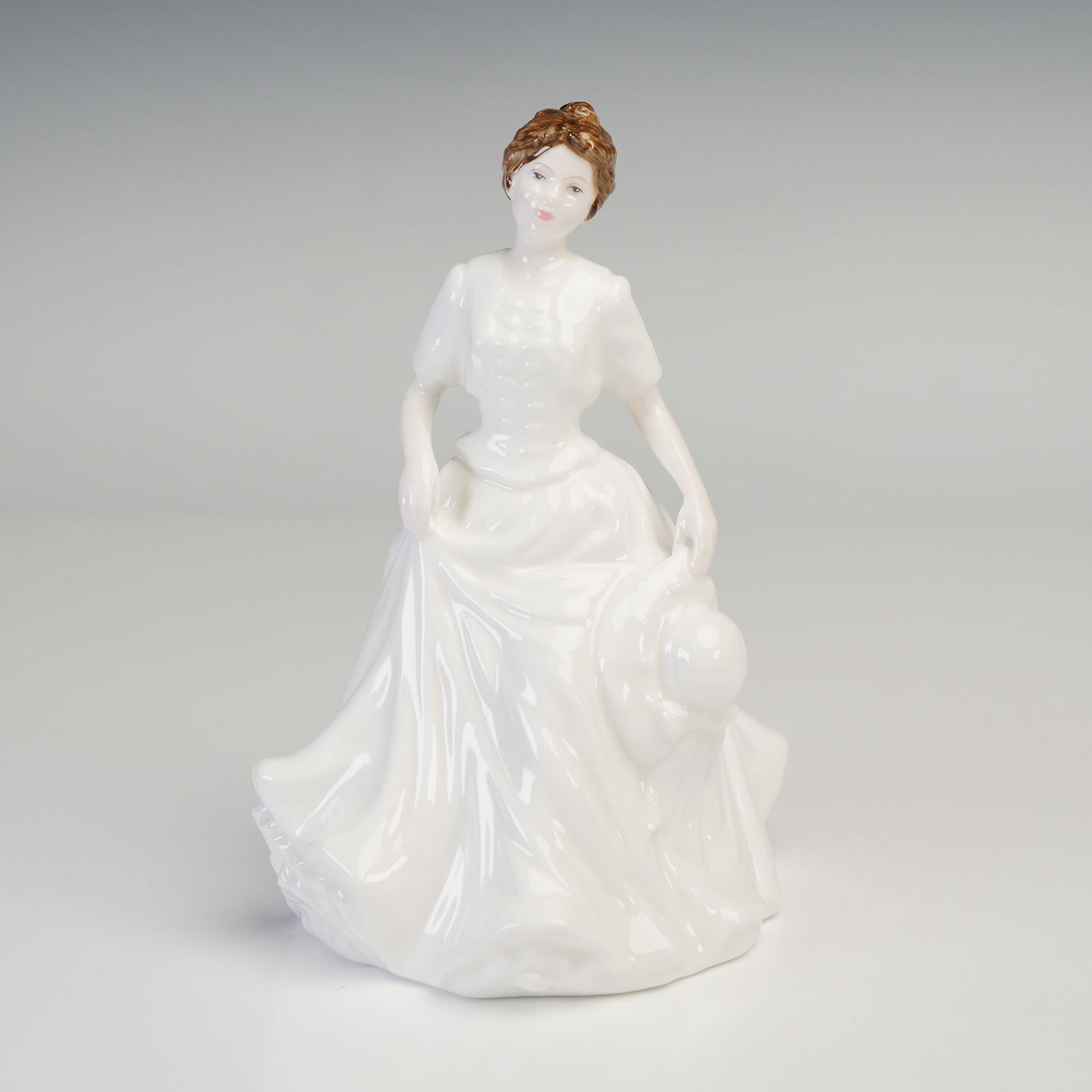 Royal Doulton Bone China Figurine, Harmony HN4096: Portraying a graceful young woman in a flowing white gown, holding a wide-brimmed hat in one hand and gathering her skirt with the other. Her refined pose and delicate facial features capture a timele