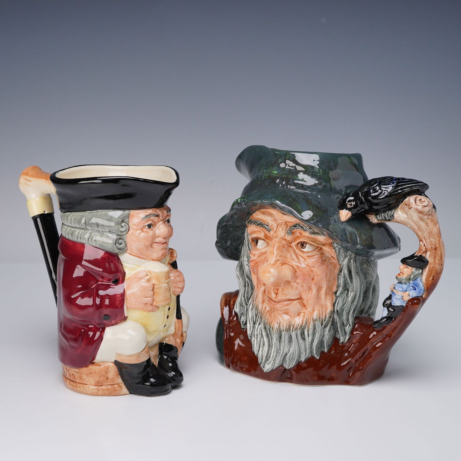 2pc Royal Doulton Character and Toby Jugs, Rip Van Winkle & Jolly Toby: A pair of Royal Doulton character jugs including Rip Van Winkle, model D6438, depicting the legendary bearded figure wearing a green hat with a handle featuring a raven and miniature figure, and Jolly