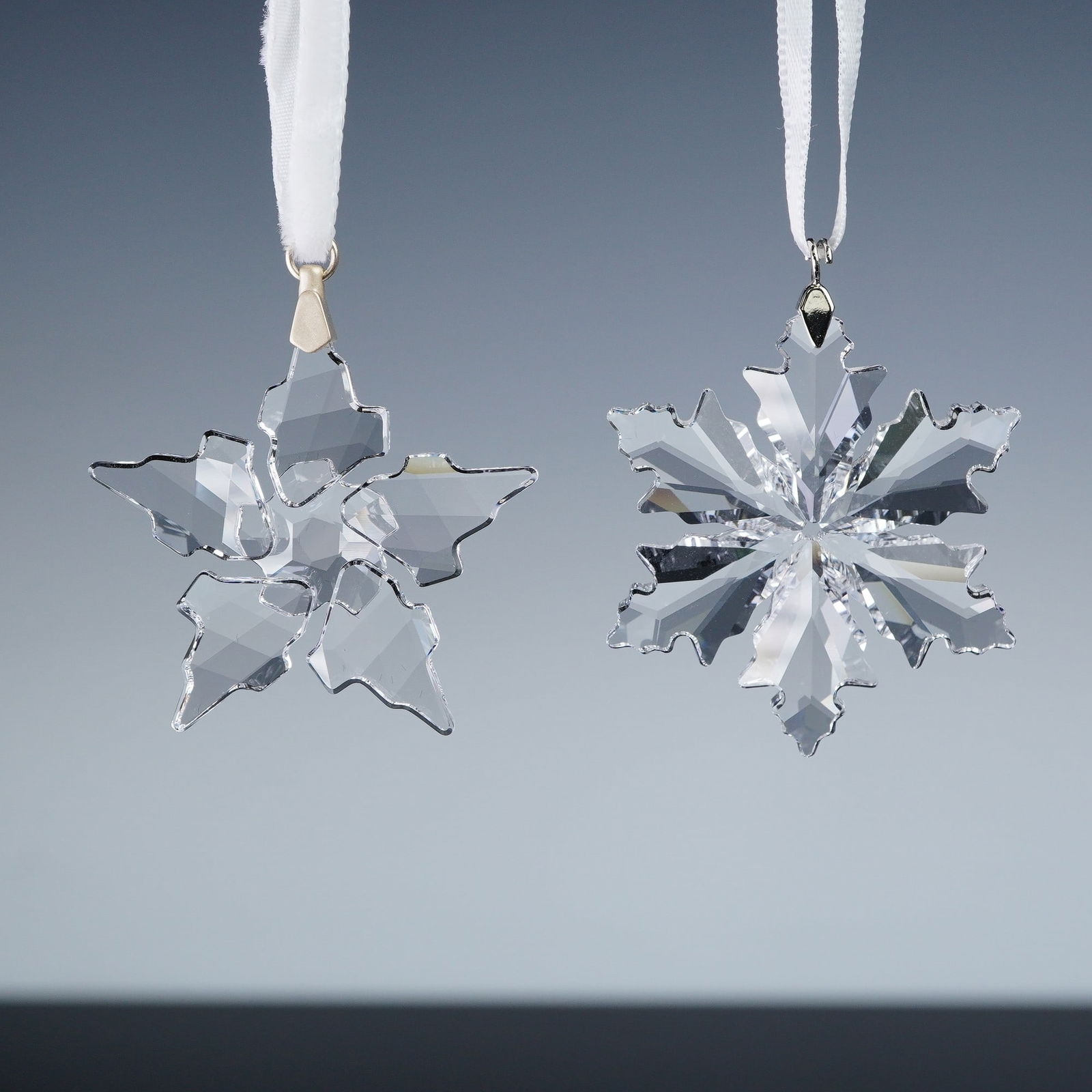 2pc Swarovski Crystal Christmas Snowflake Ornaments: Pair of Swarovski crystal ornaments. Includes the 2021 Little Christmas Ornament, number 5574358, a faceted snowflake design suspended from a white ribbon. Also features the 2014 Little Christmas Orna