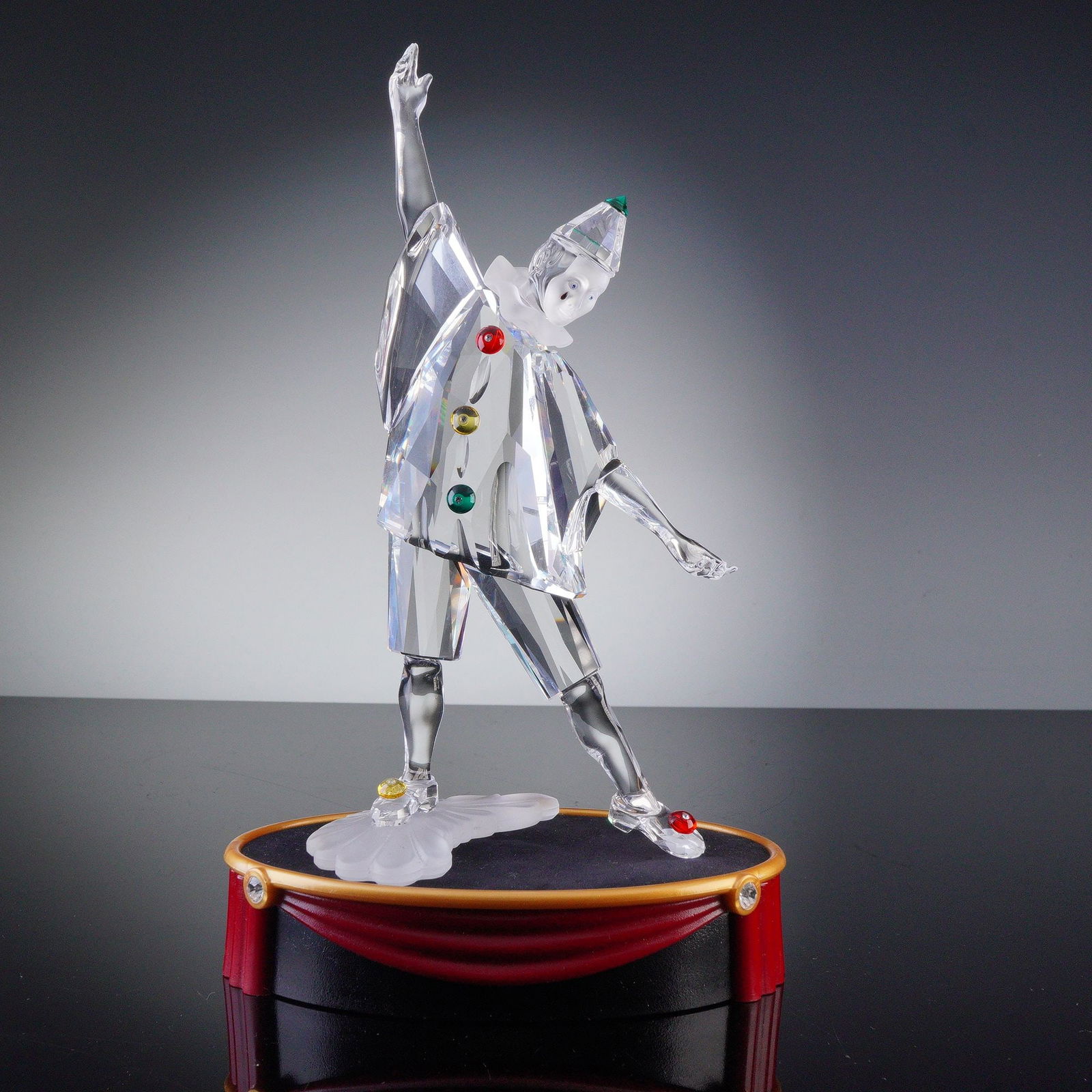 Swarovski Crystal Figurine, Pierrot Clown with Base: This beautifully crafted Swarovski Crystal Pierrot clown figurine features faceted clear crystal with colorful red, green, and yellow buttons on the costume. The whimsical figure is mounted on a red a