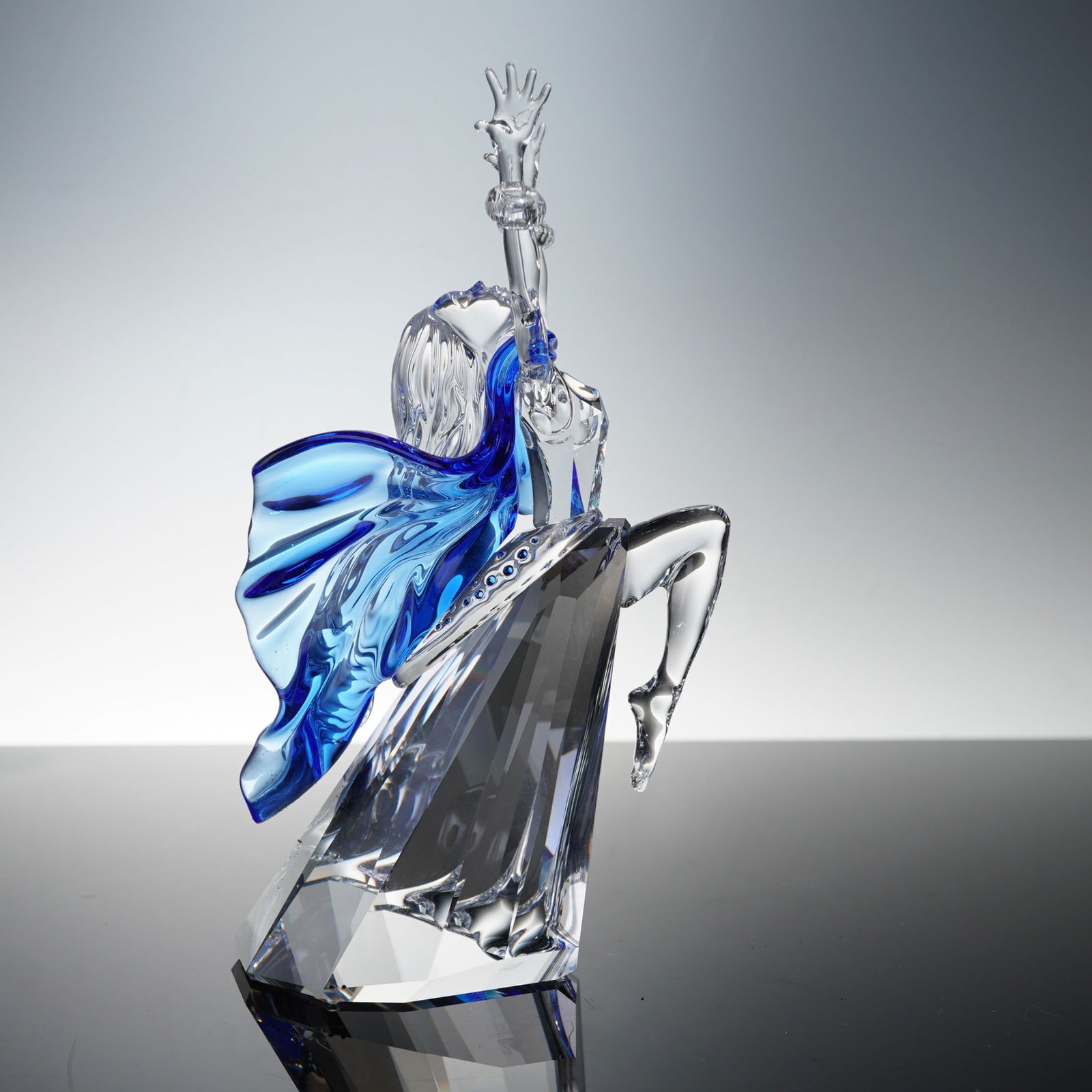 Swarovski Magic of Dance Crystal Figurine, Isadora 279648: Rendered in clear and deep blue crystal with intricate detailing that conveys elegance and movement. The figure is posed dramatically with arms raised, flowing hair, and a billowing cape of translucen