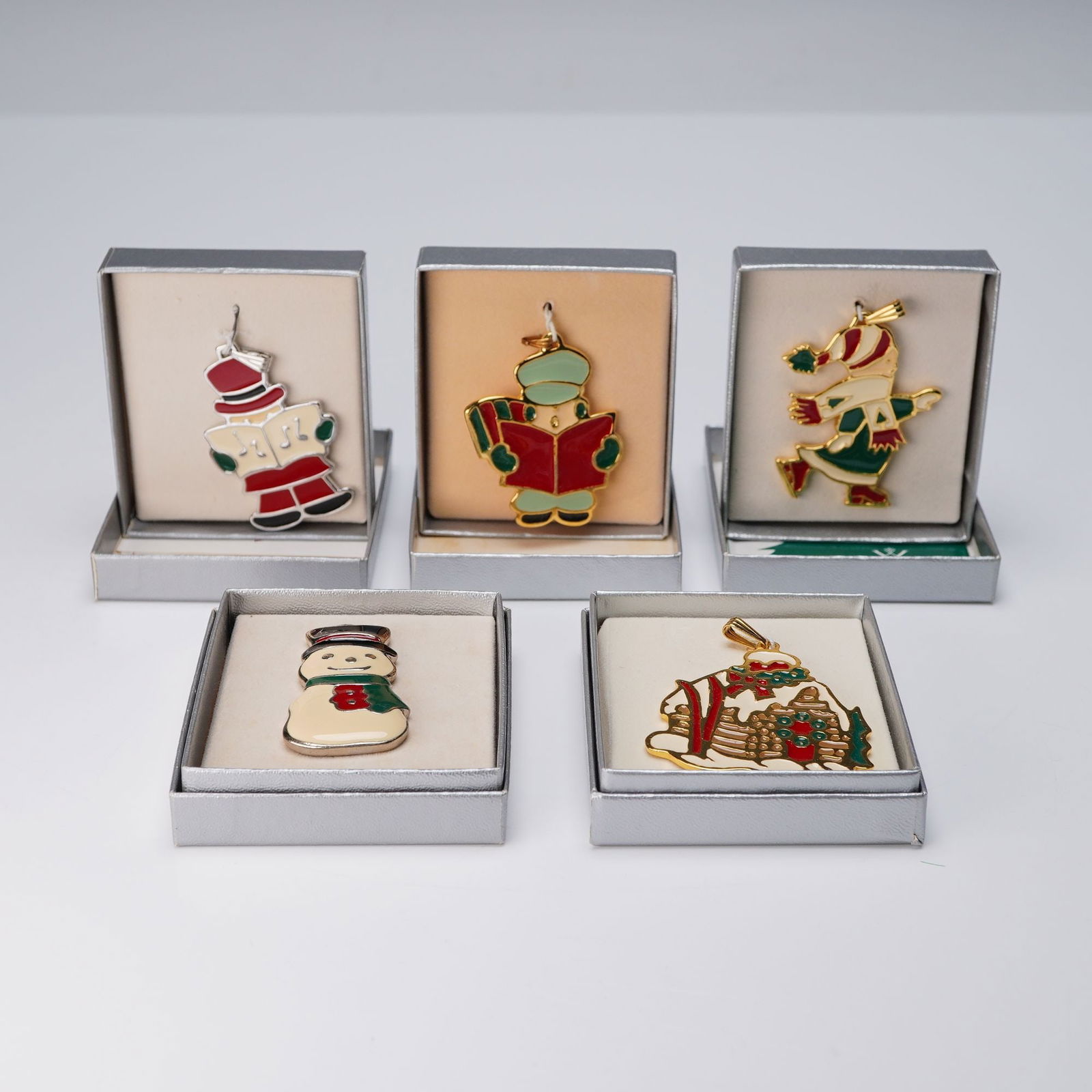 5pc Wallace Silversmiths Enameled Christmas Pendants: A charming assemblage of five gold plate and silver toned pendants with enameled accents. Included in the set are two separate carolers, a gingerbread house, an ice skater girl, and a snowman, These a