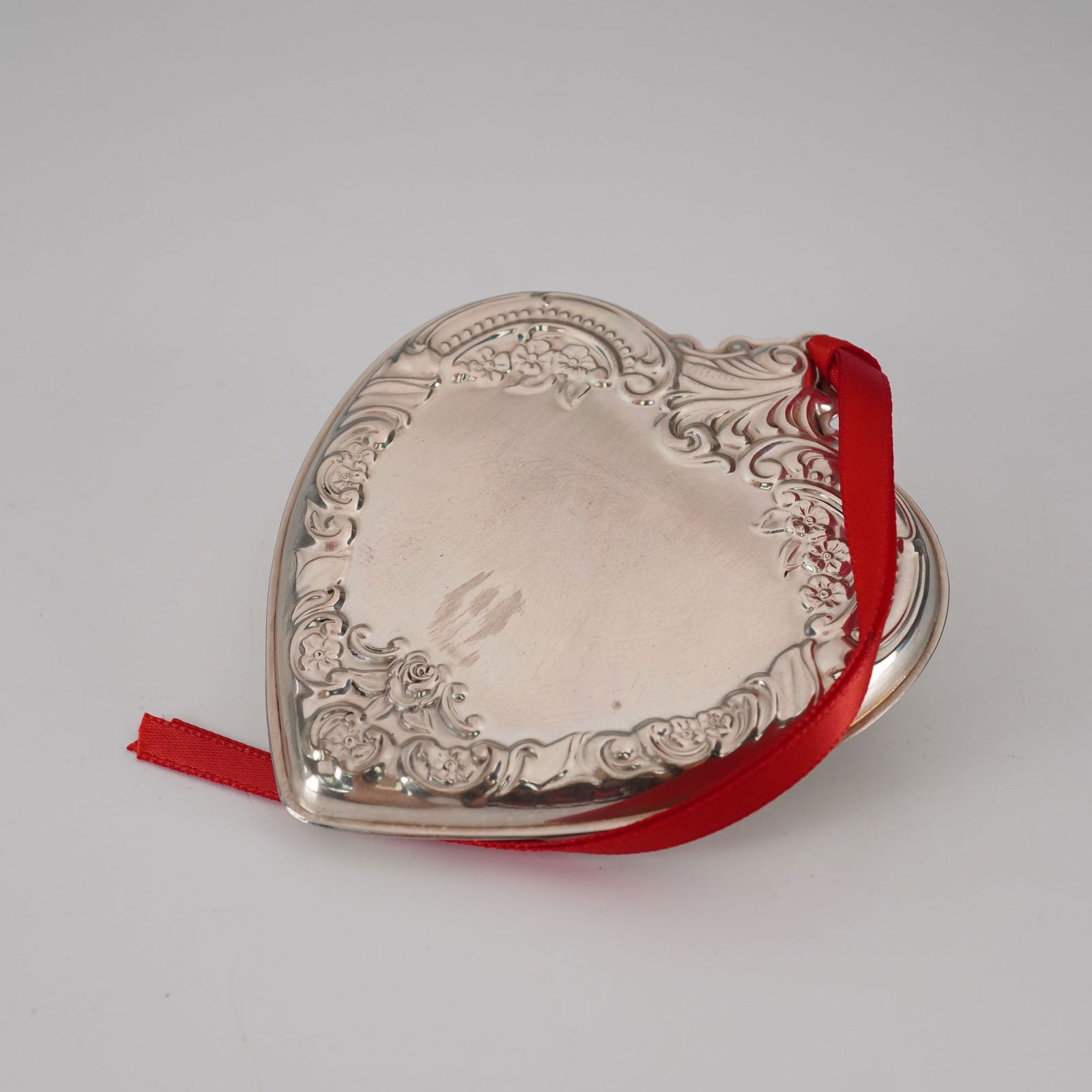 Wallace Silversmiths Sterling Silver Annual Heart Ornament: Heart ornament is finely crafted with an ornate repousse floral and scroll border surrounding a smooth central field. Marked Wallace Sterling 1992 on reverse. Includes original presentation box, red f