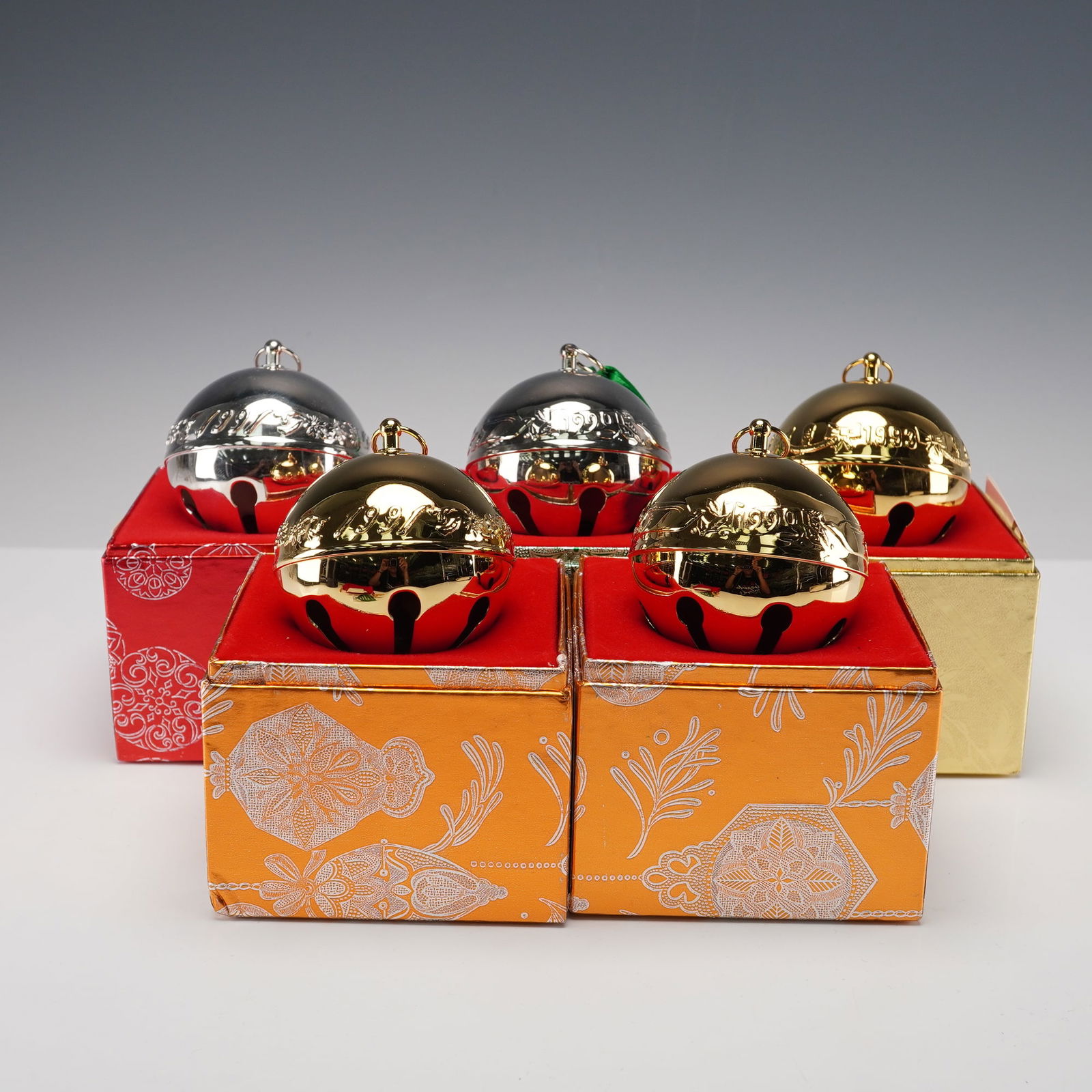 5pc Wallace Silversmiths Annual Sleigh Bell Ornaments: A collection of five Wallace Sleigh Bell Christmas ornaments, including both silver-plated and gold-toned examples. Each bell features intricate engraved decoration and comes in its original decorativ