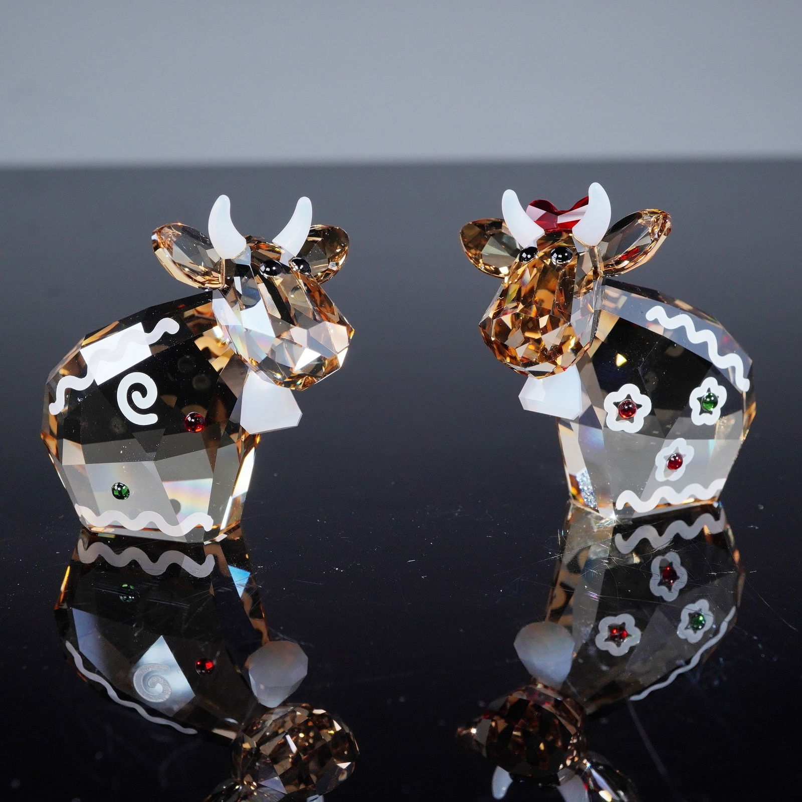 A Pair of Swarovski Crystal Mo Figurines, Gingerbread Mos, 2018: A pair of Swarovski Crystal 'Mo' figurines, identified as the 'Gingerbread Mos, Limited Edition 2018'. Each figurine is crafted from faceted amber-toned crystal, featuring opaque white horns and snout