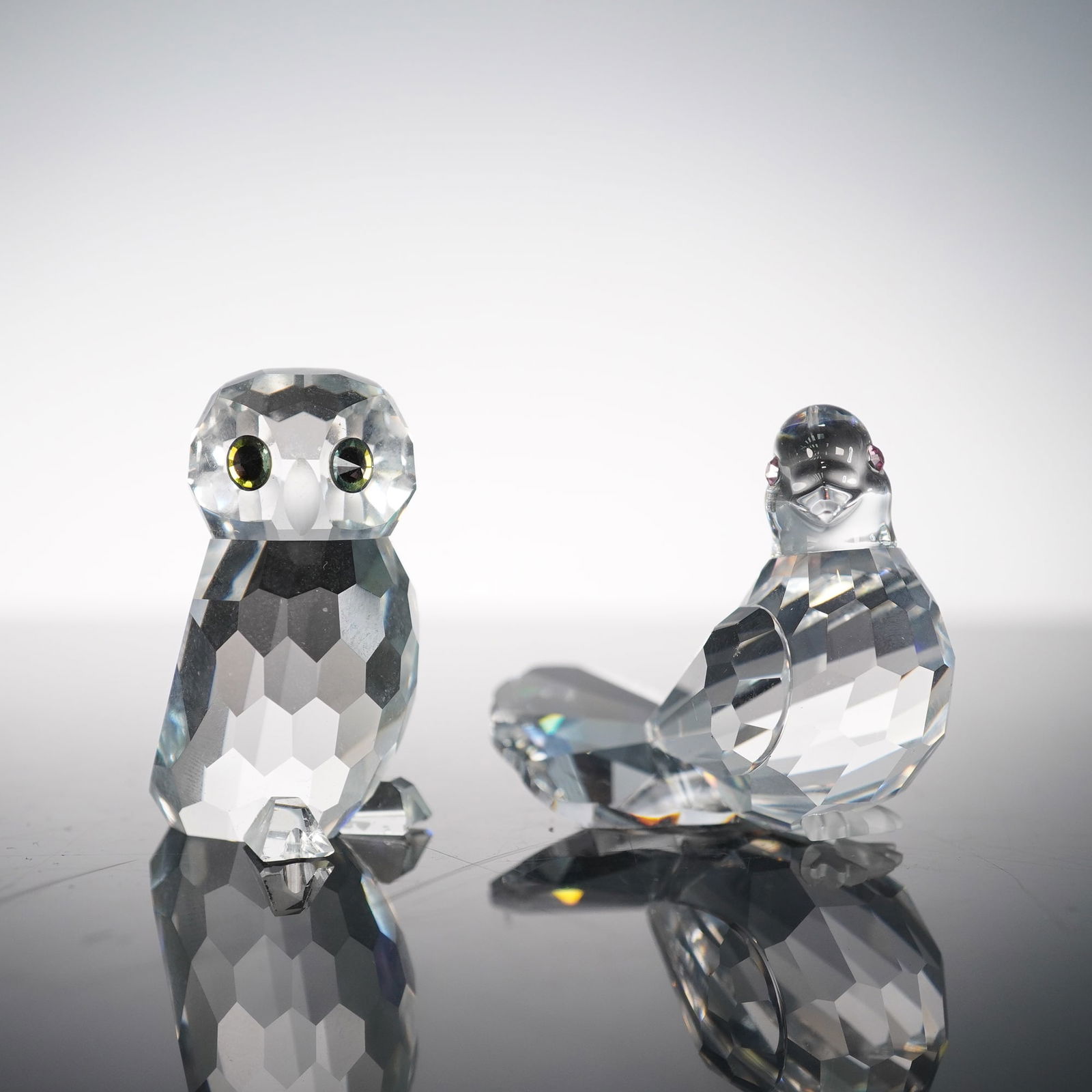 2pc Swarovski Crystal Figurines, Owlet and Dove: Swarovski crystal figurines including an Owlet designed by Anton Hirzinger and a Dove designed by Edith Mair. Both pieces feature precision-cut clear crystal bodies with faceted detail and colored cry