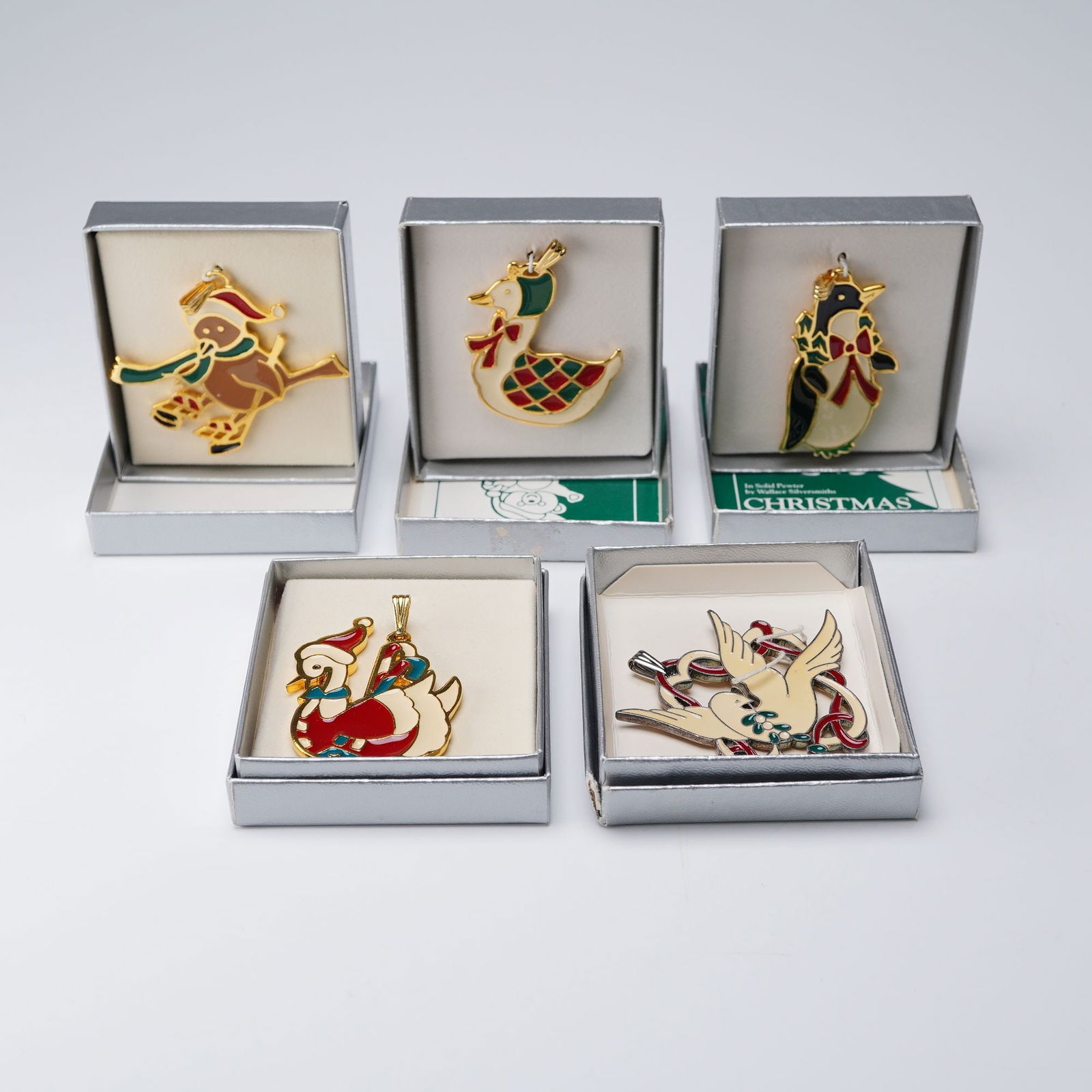 5pc Wallace Silversmiths Enameled Christmas Pendants: A collection of five enamel Christmas ornaments, each crafted in solid pewter with rich gold-tone finishes and vivid hand-painted enameling. The designs include a Penguin, a Snowbird, Mother Goose, a
