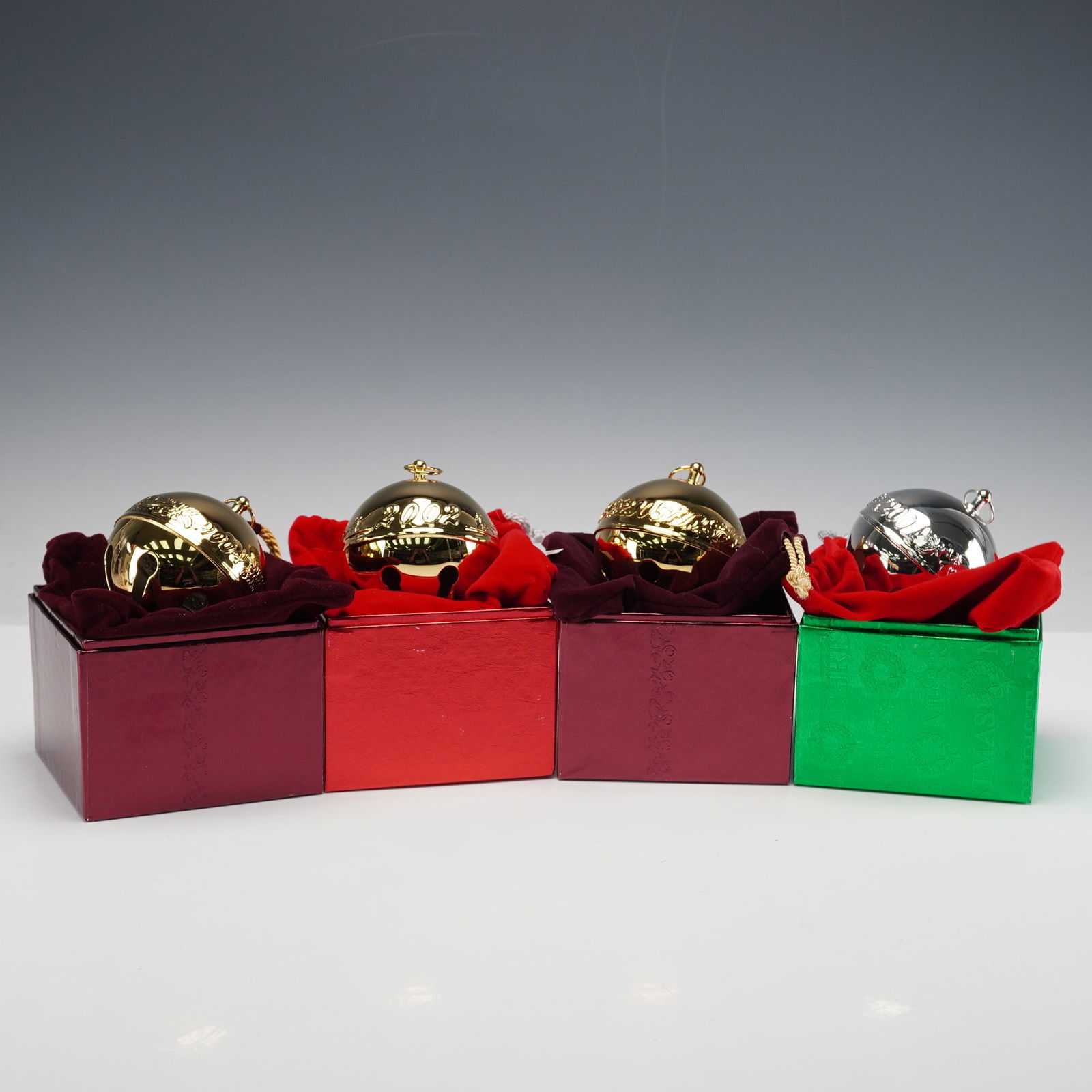 4pc Wallace Silversmiths Annual Sleigh Bell Ornaments: Set of four Wallace Silversmiths Annual Sleigh Bells Christmas ornaments, including three in gold finish and one in silver finish, each engraved with the year and presented in original velvet-lined di