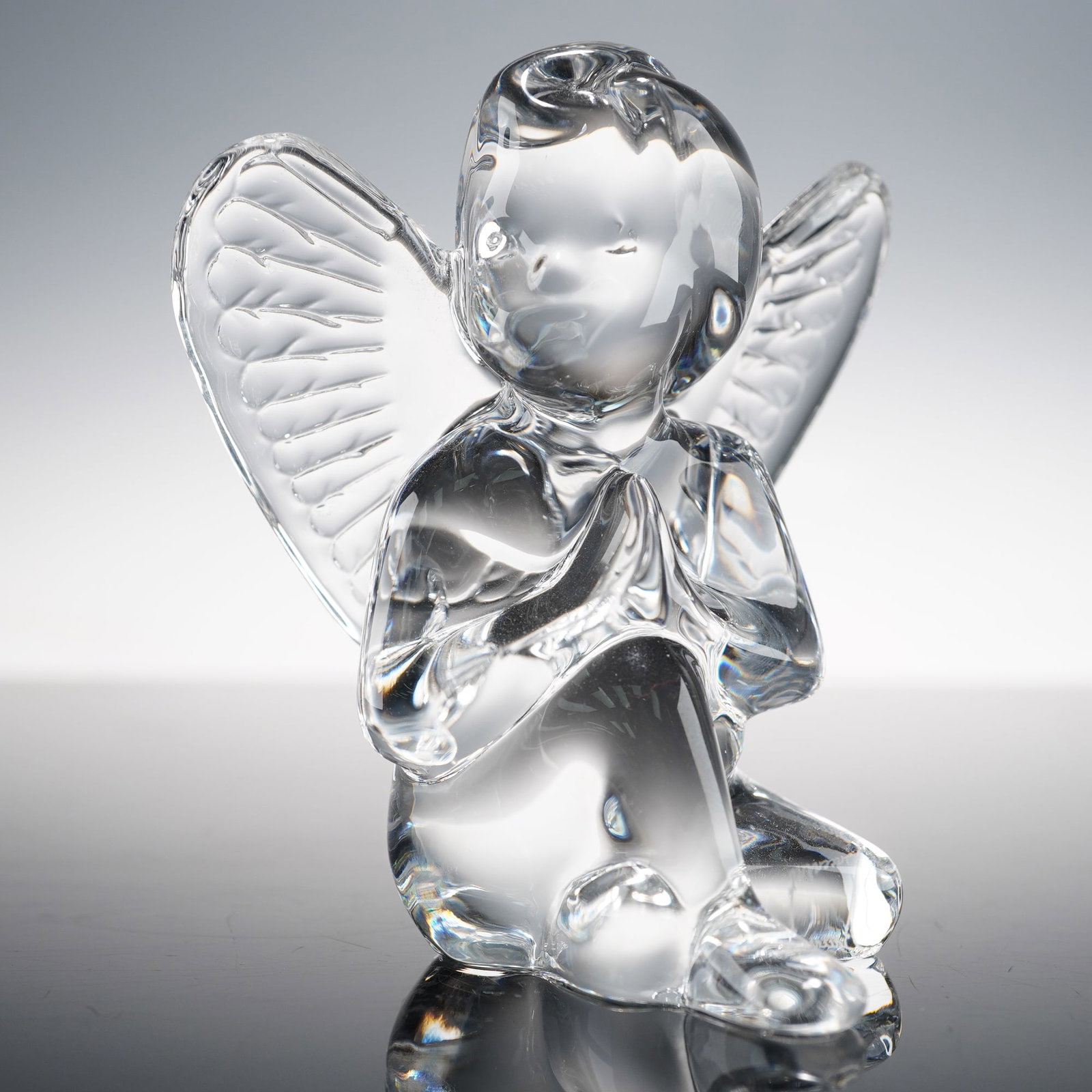 Baccarat Crystal Figurine Seated Angel: This Baccarat crystal figurine depicts a seated angel, elegantly crafted in clear, smooth crystal. The intricate details of the angel's wings and dress add to its serene beauty. The figurine's peacefu
