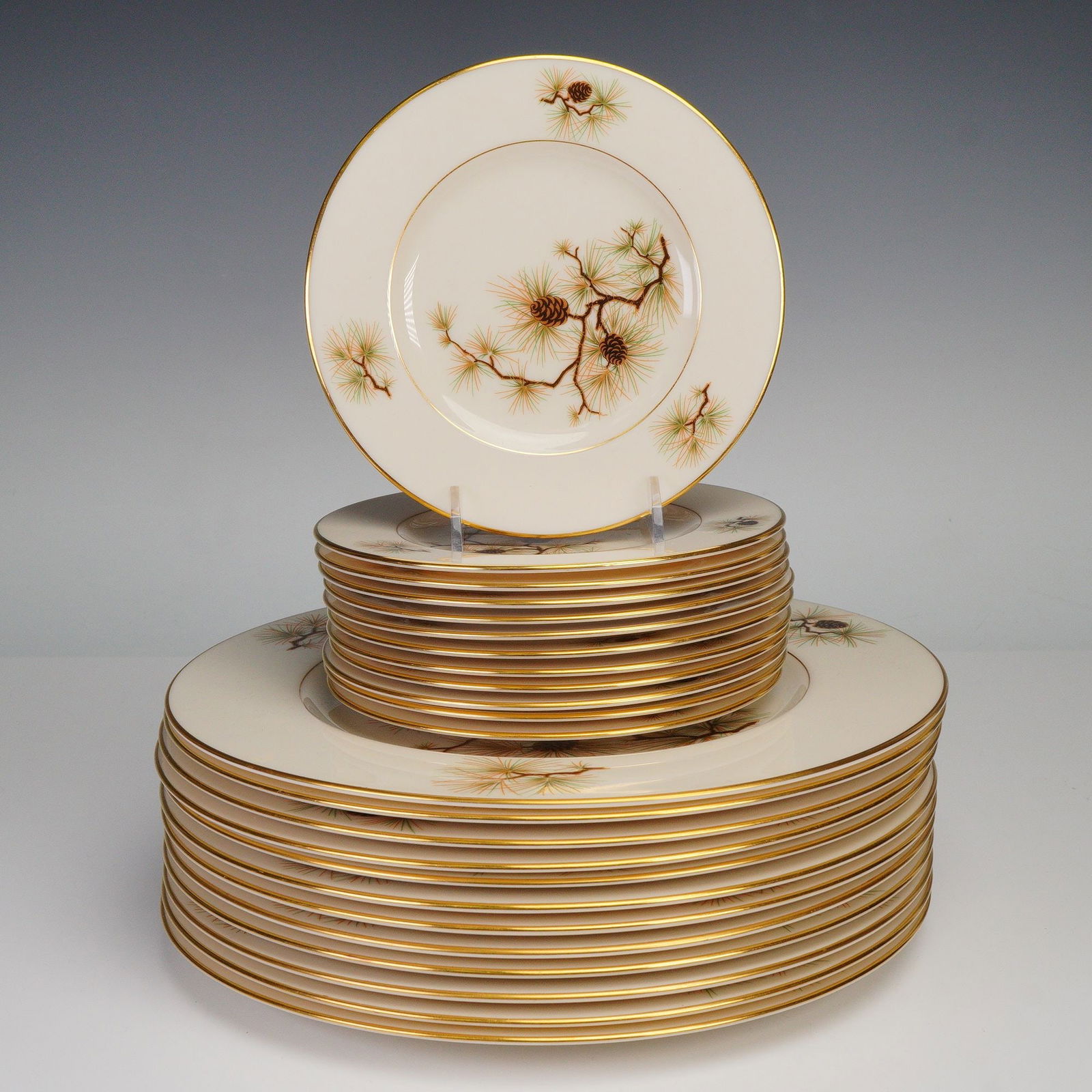 24pc Lenox Pine Salad Plates & Dinner Plates: A refined twenty-four piece porcelain dinner service featuring a delicate pine branch and cone motif rendered in natural shades of brown, green, and gold. Each piece showcases fine detail work and is