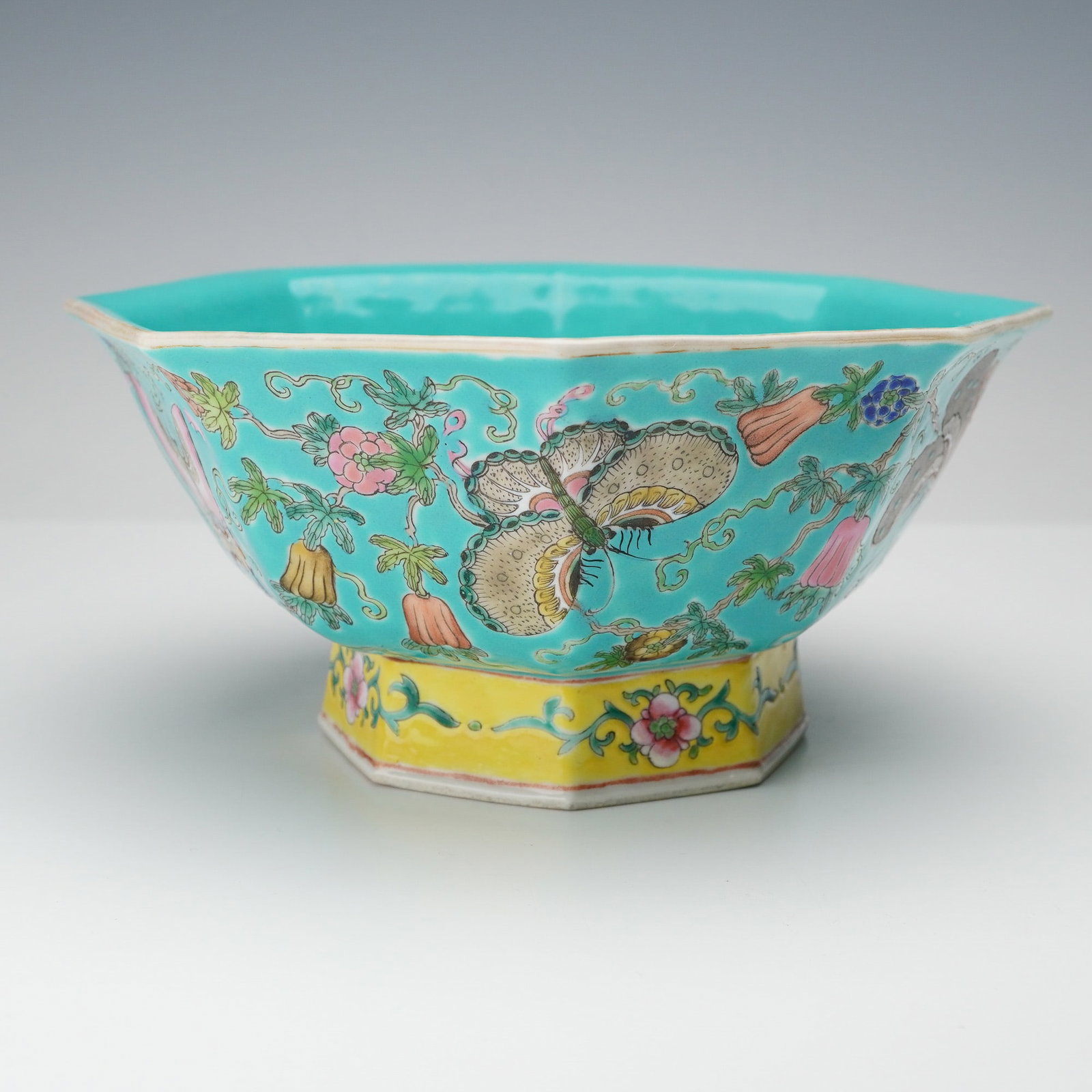 Chinese Porcelain Famille Rose-Style Lotus Bowl: An octagonal Chinese porcelain bowl beautifully decorated in the famille rose palette, featuring delicately hand-painted butterflies and blossoming flowers amidst scrolling foliage on a turquoise grou