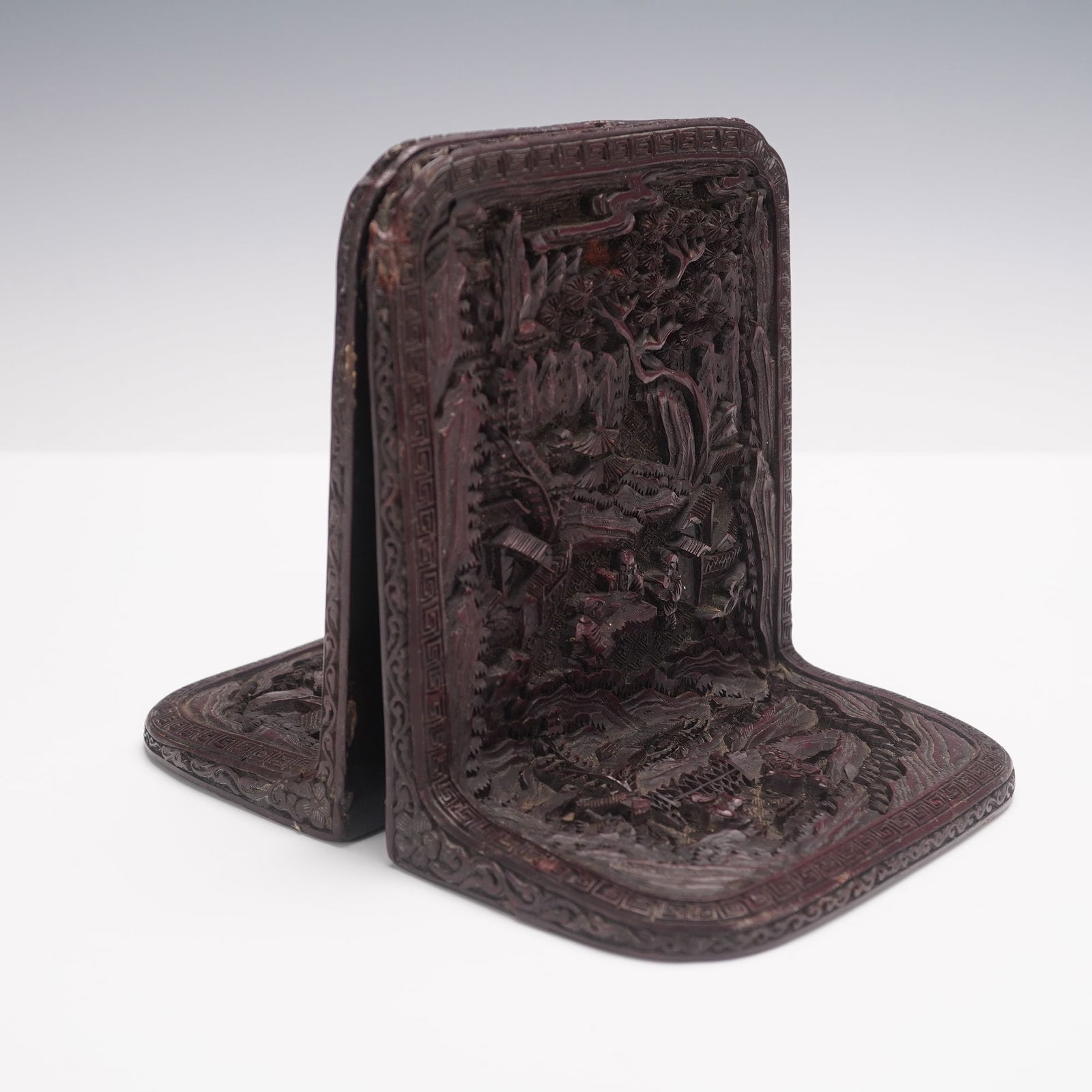 Vintage Chinese Cinnabar Lacquer Scenic Bookends: Each crafted in an L-shape with intricately carved relief scenes. The fronts display finely detailed landscapes with pavilions, figures, trees, and mountains bordered by geometric and floral patterns,