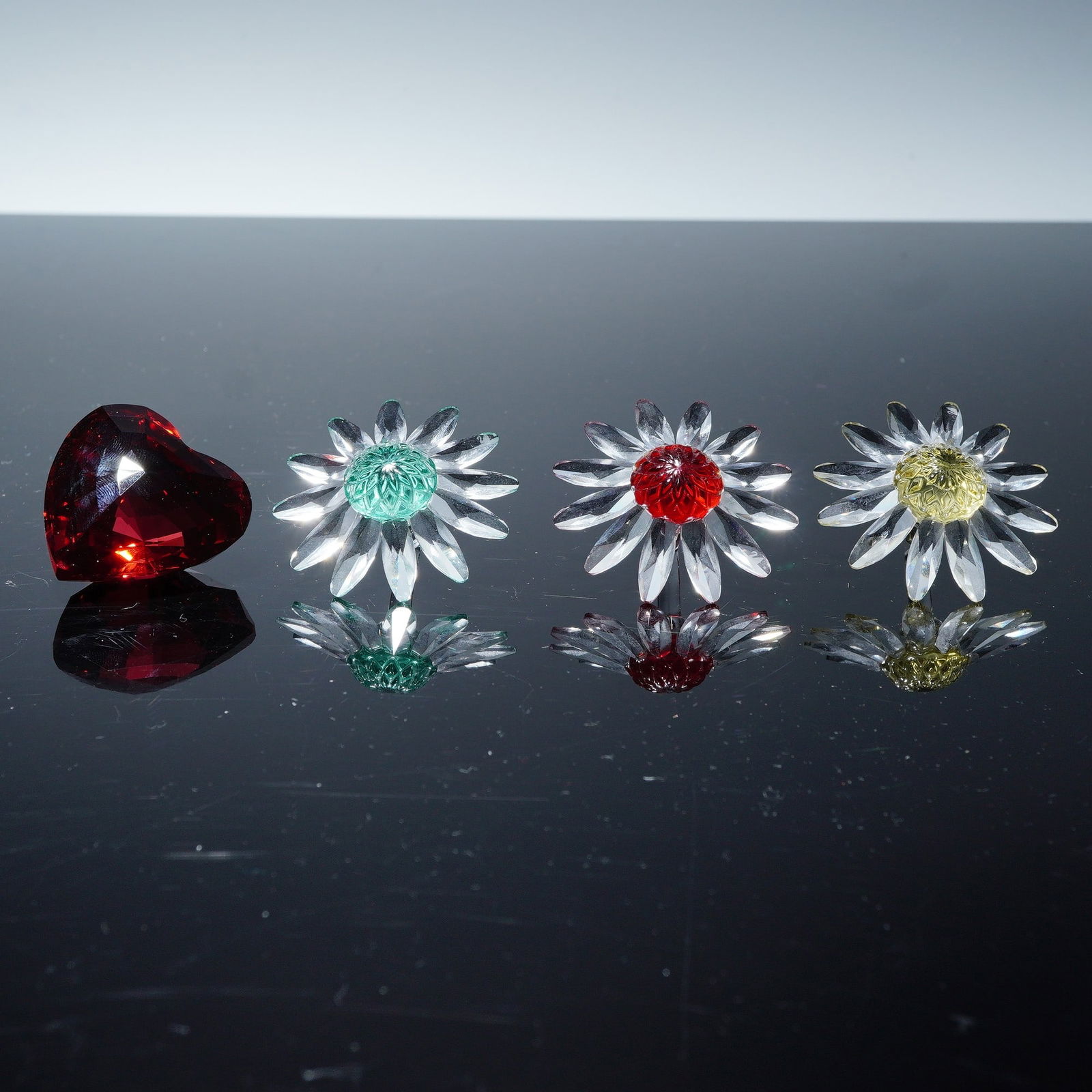 4pc Swarovski Crystal Gift Renewal Figurines, Marguerites and Red Heart: A delightful collection of Swarovski crystal, featuring a trio of Marguerite flowers and the 1998 Renewal Gift Heart in red. The flowers are crafted with precision cut clear faceted petals and vibrant