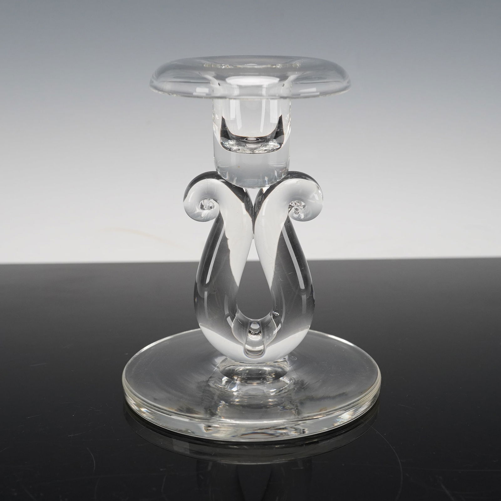 Steuben Clear Crystal Candle Holder, Scroll-Shaped Stem: A clear crystal candlestick by Steuben, crafted with the brand's hallmark clarity and precision. The piece features an elegant sculptural design with graceful, curving scroll-like elements rising from