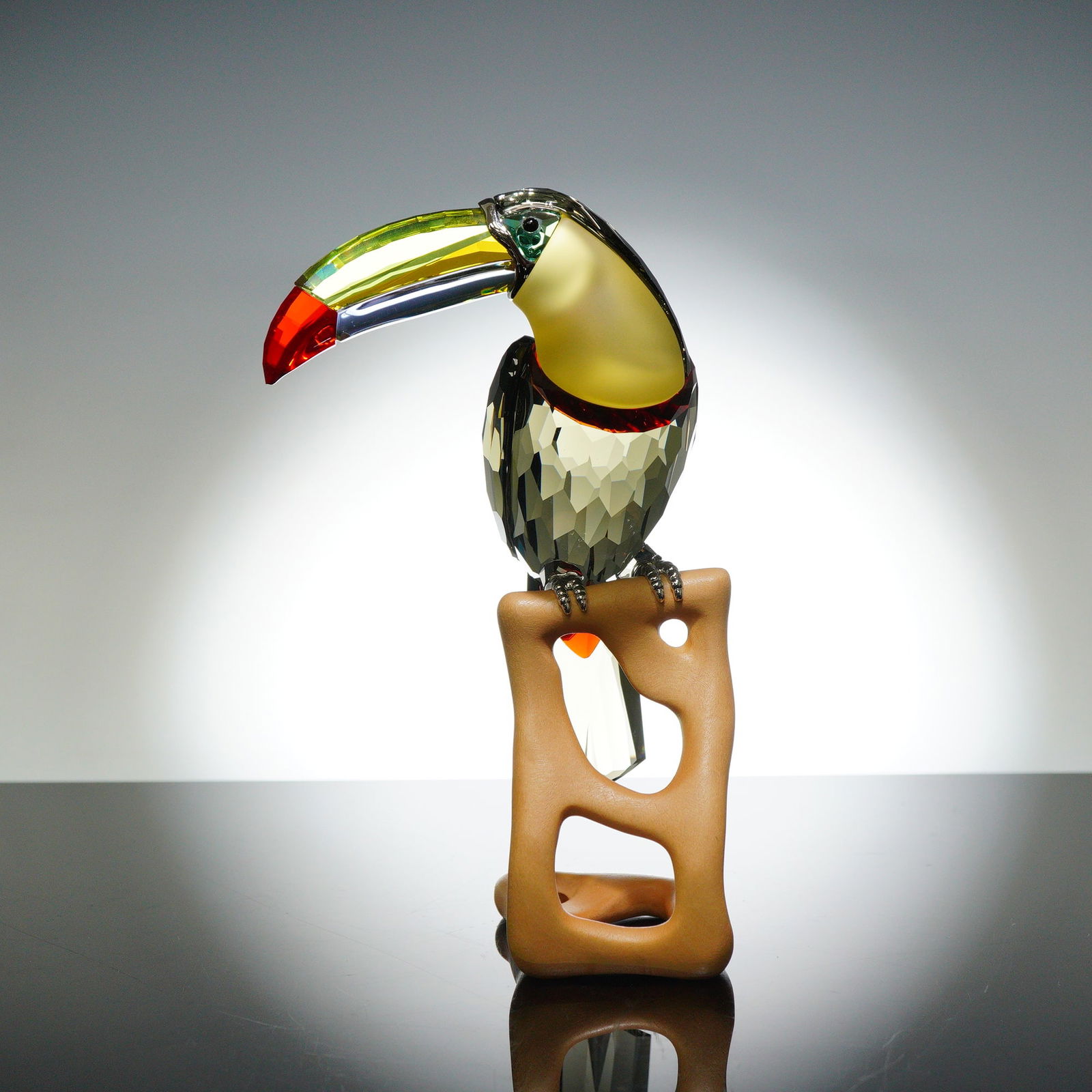 Swarovski Crystal Paradise Bird Figurine, Toucan Black Diamond: This striking sculpture, designed by Roland Schuster, features a faceted Black Diamond crystal body with an iridescent multicolored beak in vibrant yellow, green, and red tones. The bird perches grace
