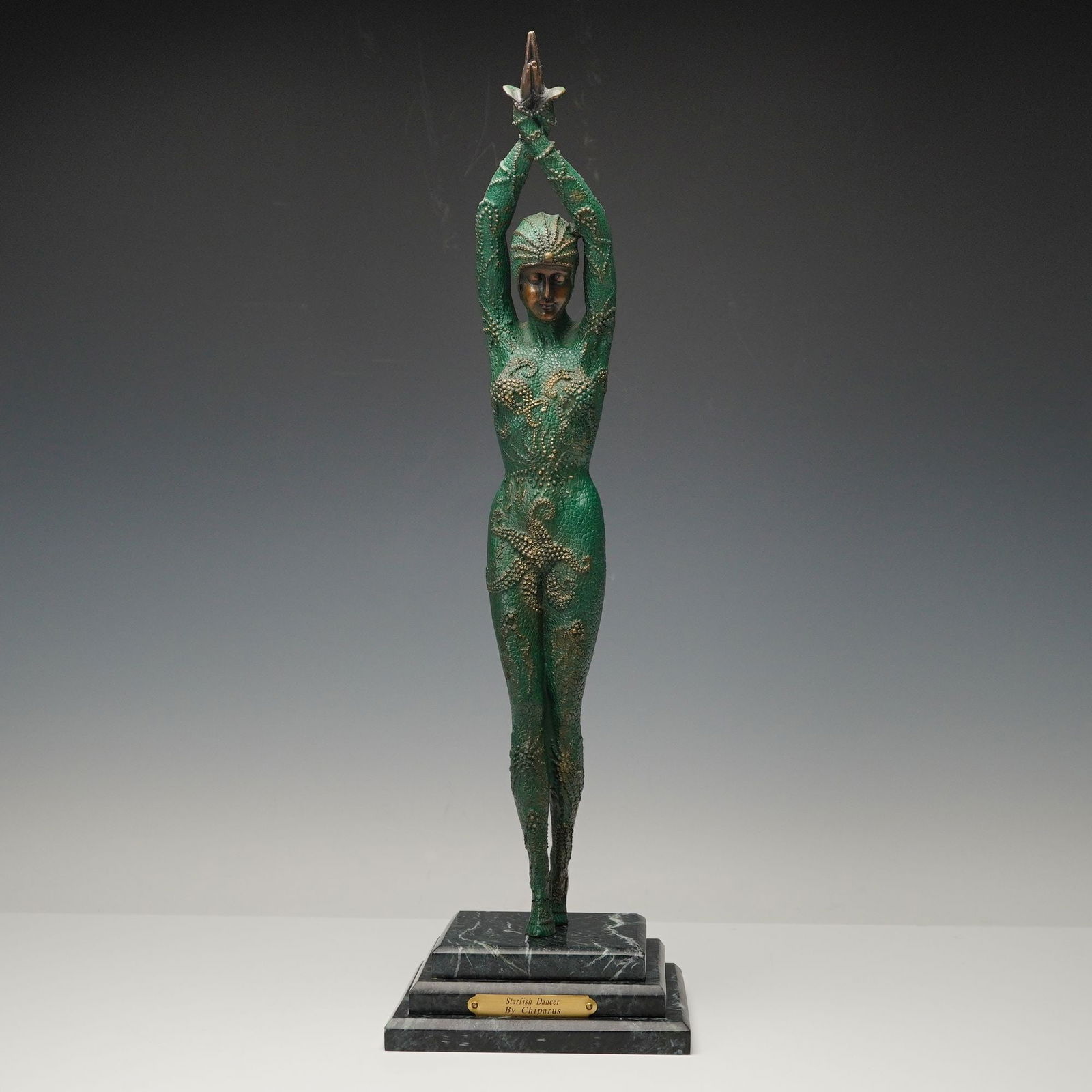 After Demetre Chiparus Bronze Starfish Dancer Sculpture on Marble Base: Elegant bronze sculpture after Demetre Chiparus (Romanian, 1886-1947) titled Starfish Dancer, depicting a poised female figure standing with arms raised gracefully overhead. The figure is adorned in a