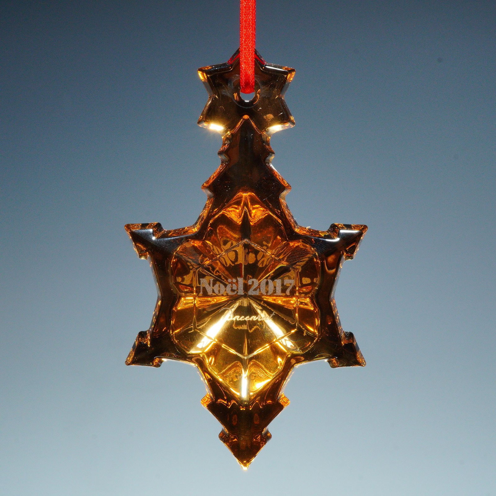 Baccarat Crystal Annual Ornament, Amber Star 2017: This exquisite Baccarat ornament from the Noel 2017 collection captures the brand's renowned artistry in fine crystal craftsmanship. Formed in a radiant amber hue, the ornament takes the shape of a fa