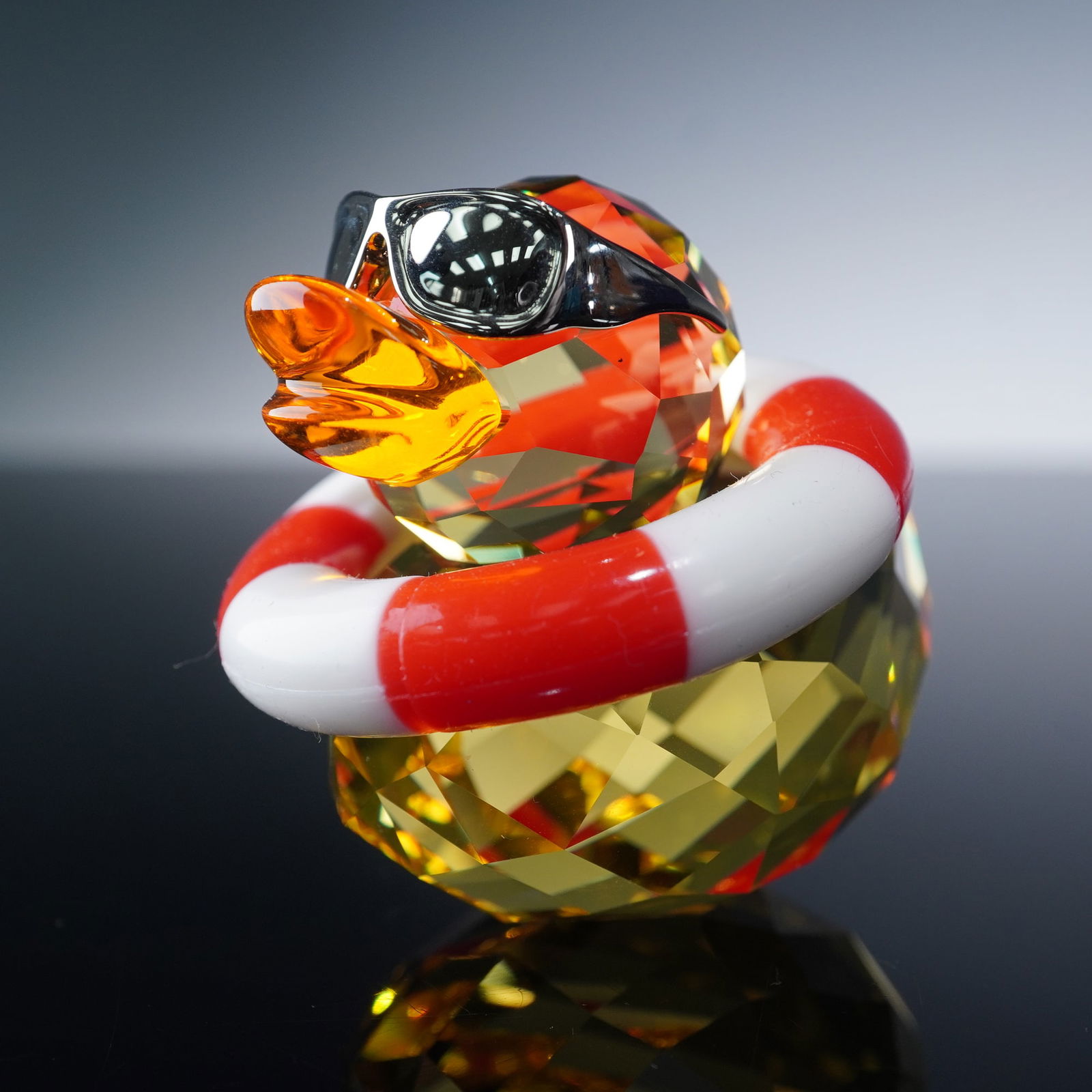 Swarovski Crystal Happy Duck Figurine, Sunny Sam: This playful duck is part of a range of happy and cheerful messengers of positive emotions. Sunny Sam is made of yellow crystal body with red and white silicone life belt. He wears a pair of metal rem