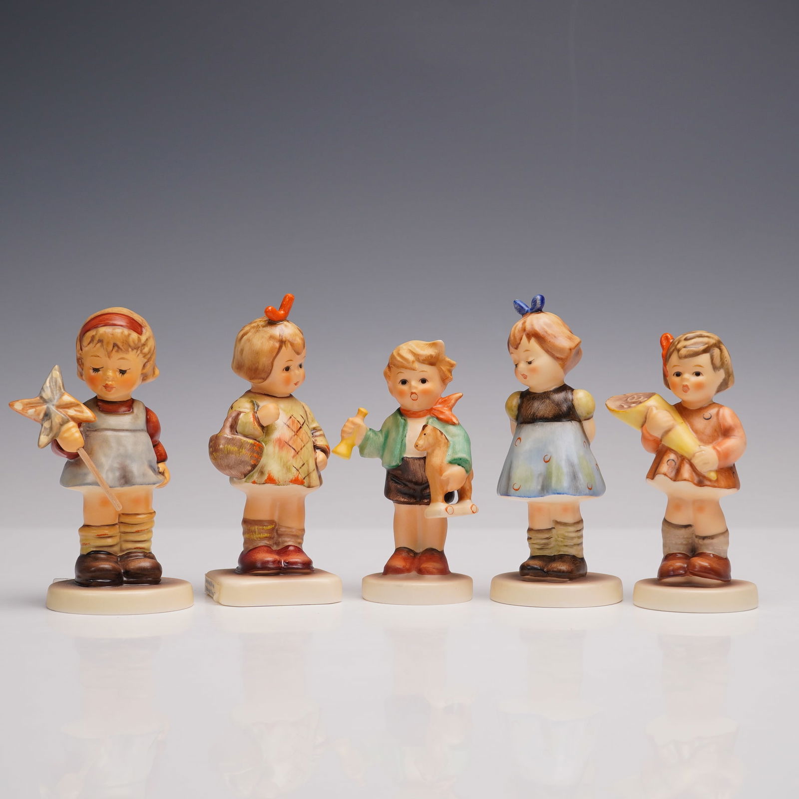 5pc Goebel Hummel Porcelain Figurines: A set of five porcelain figurines, each hand-painted in delicate hues and modeled to depict children in whimsical poses. Figures included are A Sweet Offering, Two Hands, One Treat, All By Myself, I B