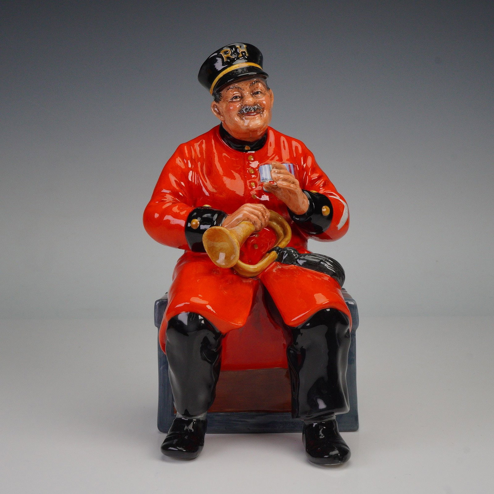 Royal Doulton Figurine, Past Glory HN2484: This Royal Doulton figurine, Past Glory, captures the charm of a jovial Beefeater guard, casually sitting with his horn in one hand and a cup in the other. The piece features rich detailing with vibra