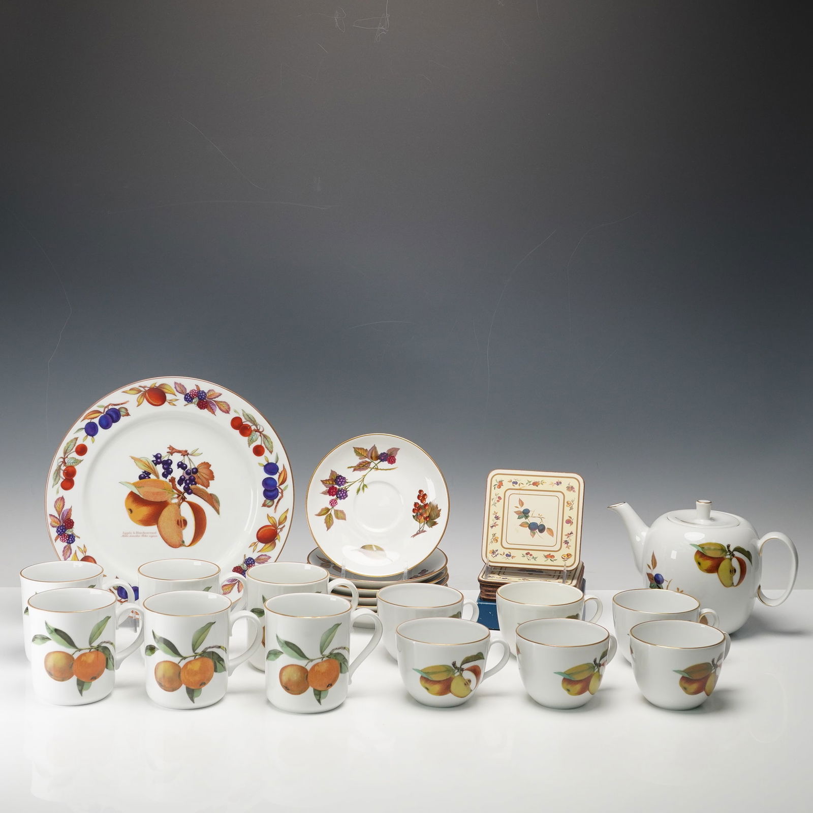 21pc Royal Worcester Porcelain Tea Set, Evesham: A charming porcelain tea service, totaling twenty-one pieces. The set includes a teapot, six cups and saucers, six mugs, a round serving plate, and a boxed set of six coasters. Each piece is adorned w