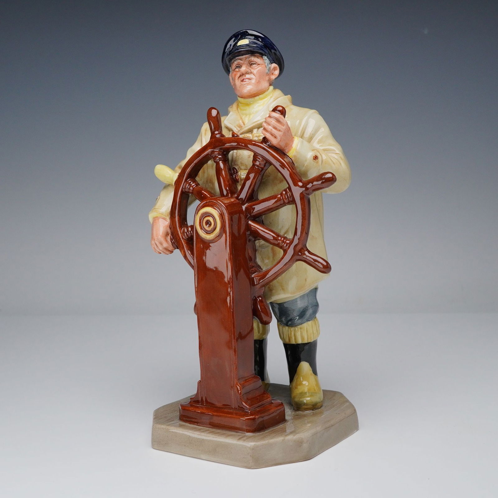Royal Doulton Figurine, Helmsman HN2499: This hand-painted figure portrays a confident seafarer at the ship's wheel, dressed in a yellow raincoat, navy cap, and sea boots, capturing the spirit of maritime adventure. Part of Royal Doulton's S