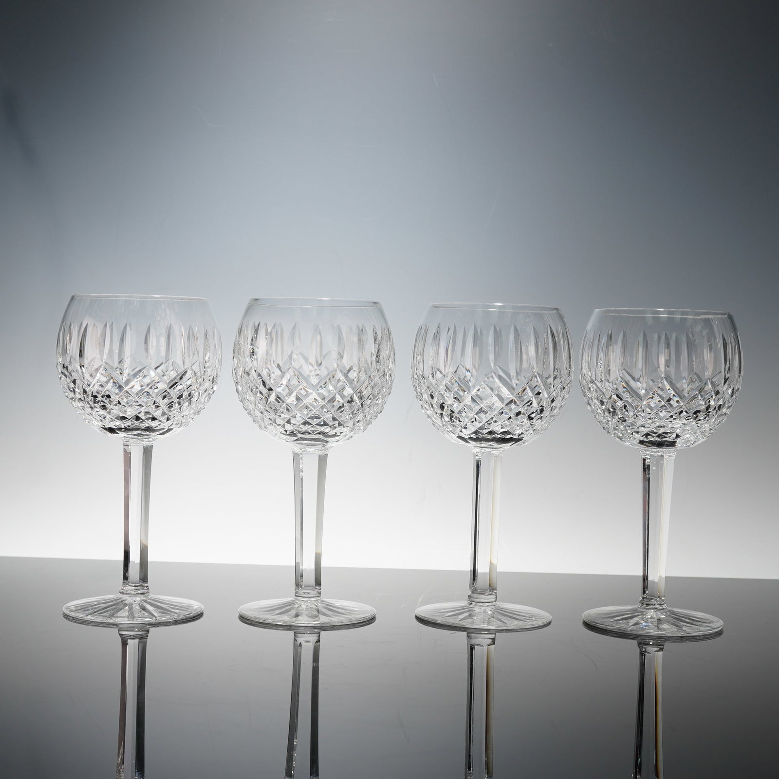 4pc Waterford Crystal Balloon Wine Glasses, Lismore: A fine set of four Waterford crystal wine glasses, each with a rounded bowl intricately cut with a diamond and vertical panel pattern, raised on slender faceted stems and circular bases. Each glass be