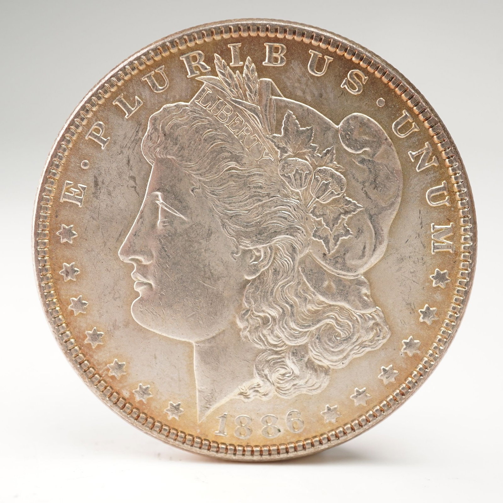 1886 Morgan Silver Dollar: The obverse displays a left-facing portrait of Lady Liberty wearing a Phrygian cap adorned with cotton and wheat, symbols of agricultural strength. Surrounding her are the inscriptions E PLURIBUS UNUM