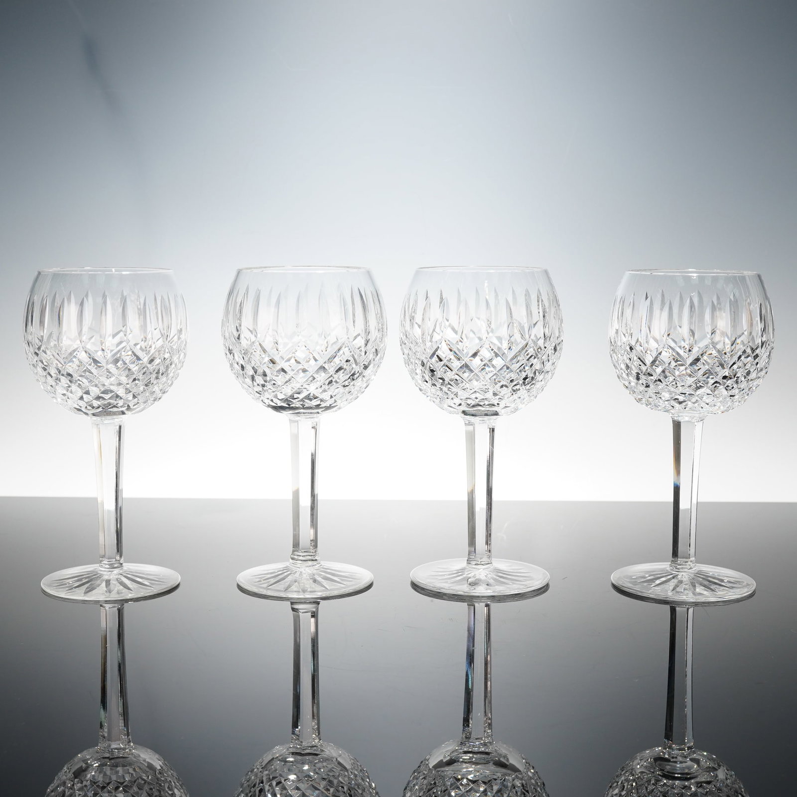 4pc Waterford Crystal Hock Wine Glasses, Lismore: A refined set of four cut crystal balloon wine glasses, each elegantly crafted by Waterford. These glasses feature a rounded bowl with intricate diamond and vertical cuts that create a striking interp
