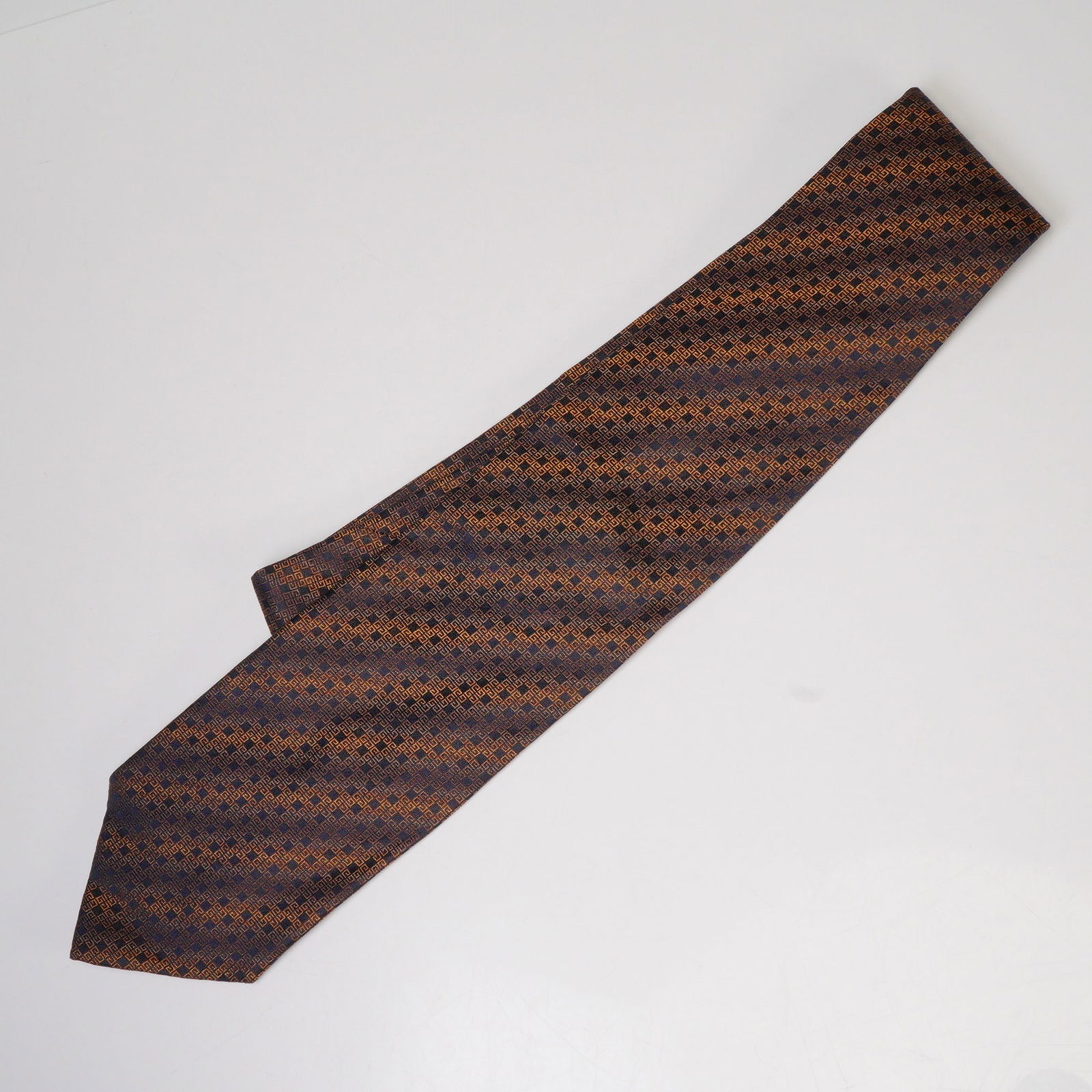Givenchy Paris Silk Tie, Geometric Pattern: Givenchy Paris silk tie made in Italy, featuring an intricate geometric pattern in shades of bronze and navy blue. The design displays a repeating square motif woven into the fabric, giving the tie a