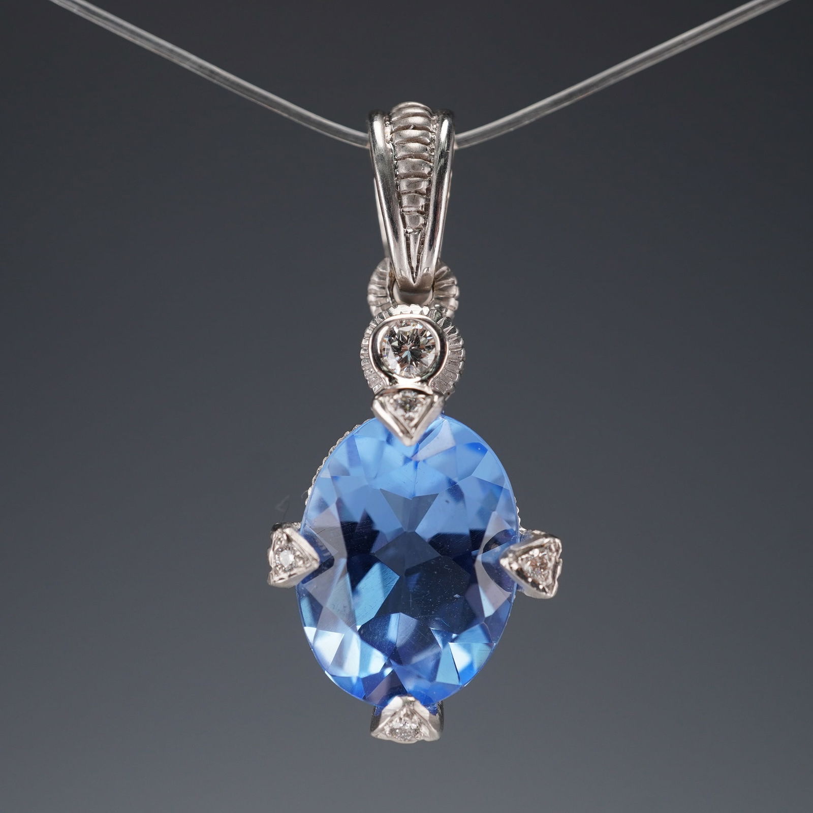 Judith Ripka 18K White Gold Blue Stone and Diamond Pendant: Oval faceted blue gemstone set in an 18K white gold mount with diamond-accented prongs and bail. Marked 18K on reverse. Includes black velvet pouch. Weight: 6.7 g. Dimensions: 1.25"H x 0.5"W x 0.5"D C