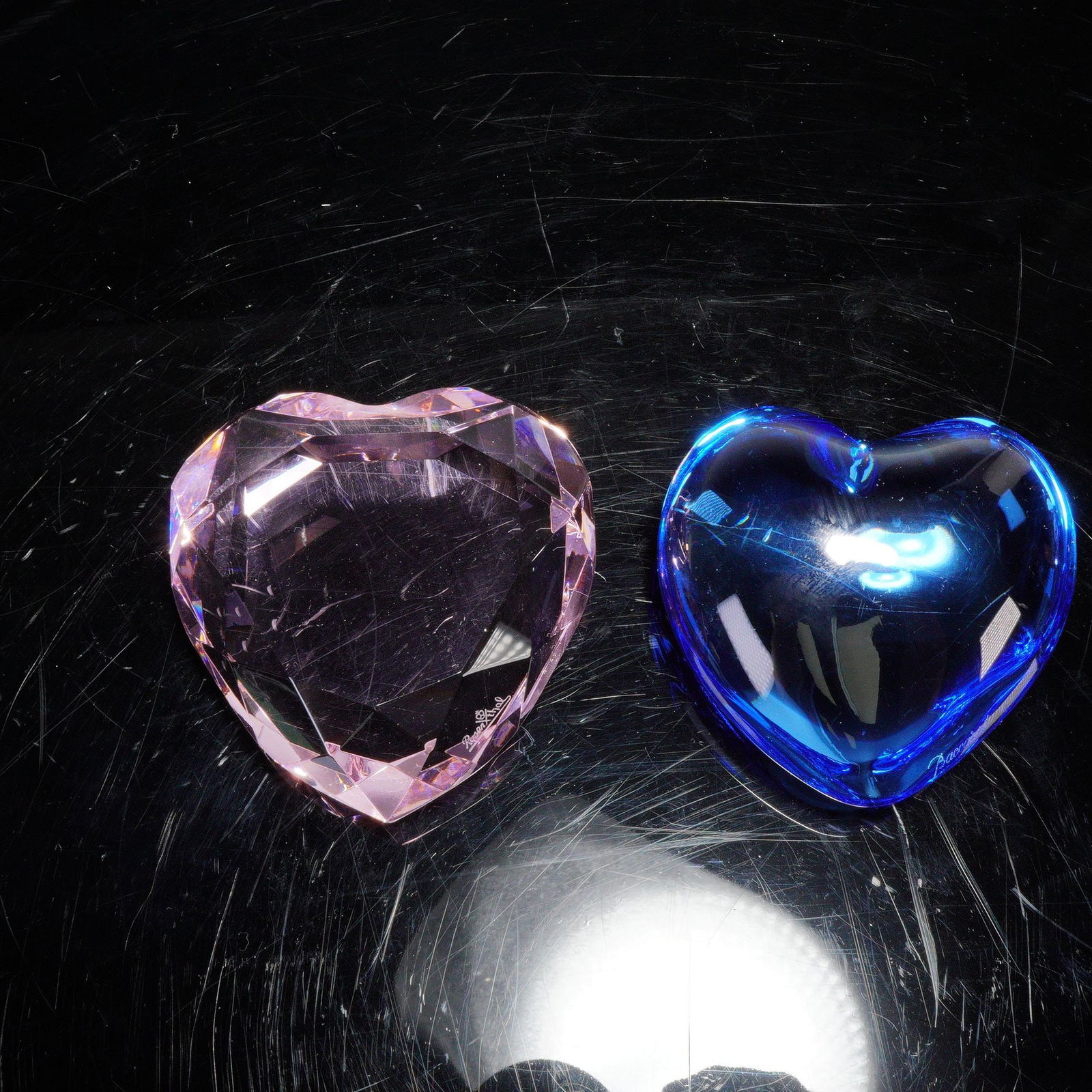 2pc Rosenthal and Baccarat Crystal Heart Paperweights: Two crystal heart paperweights comprising one by Rosenthal in light pink faceted crystal with a multi-angled cut resembling a gemstone, and one by Baccarat in cobalt blue crystal with a smooth rounded