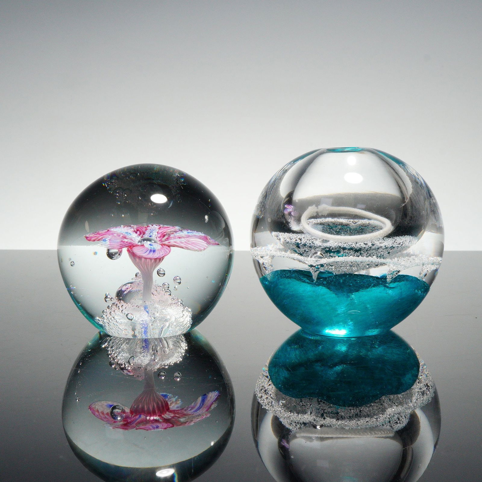2pc Art Glass Paperweights, Teal and Pink Floral: Pair of spherical art glass paperweights including an Artcristal Bohemia crystal example handmade in Czech Republic with teal interior and controlled bubbles, together with a pink flower and bubble de