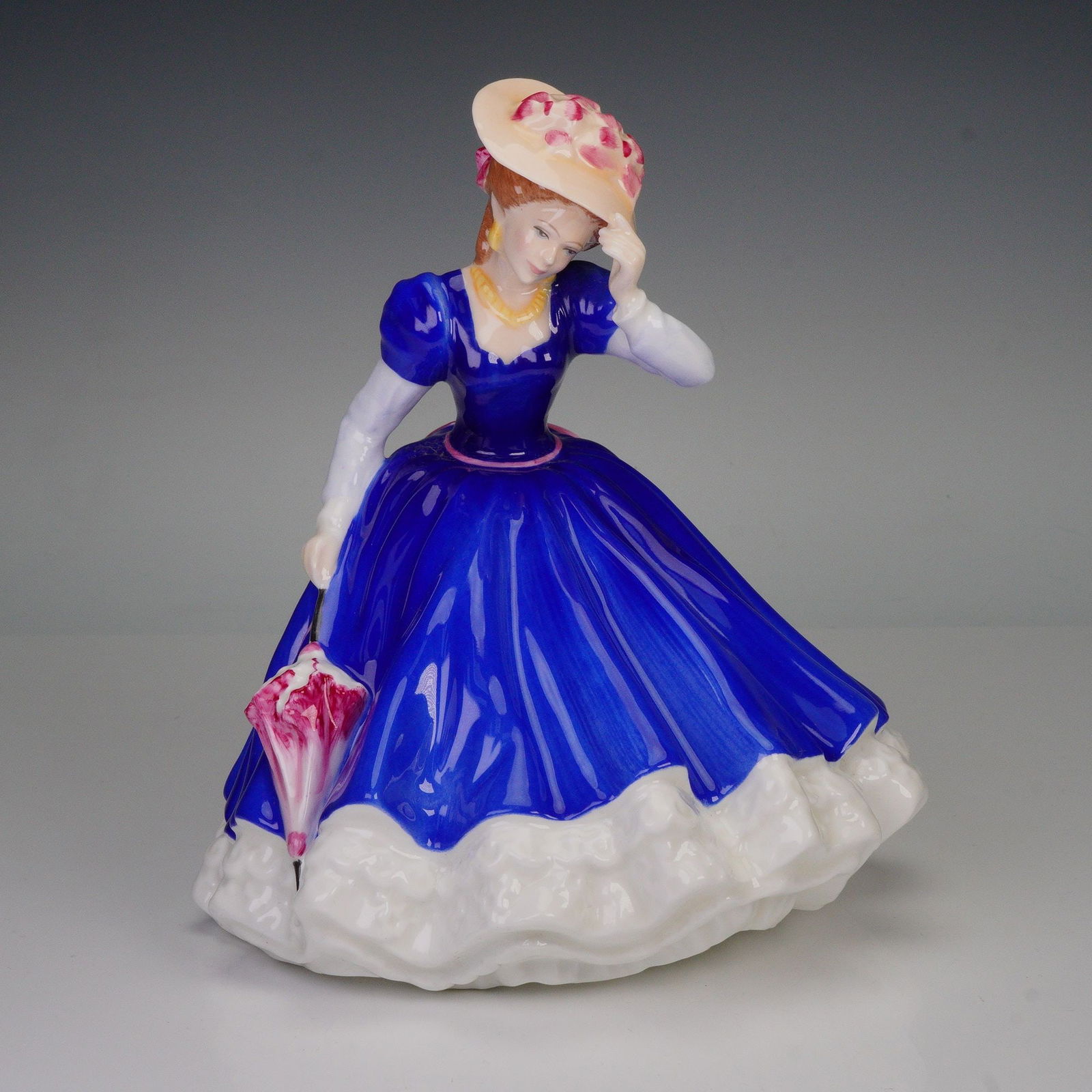 Royal Doulton Figurine, Figure of the Year Mary HN3375: This Royal Doulton figurine Figure of the Year Mary (HN3375) depicts a woman in a blue gown with detailed accents on her dress, hat, and parasol. Released as part of the Figure of the Year series, it
