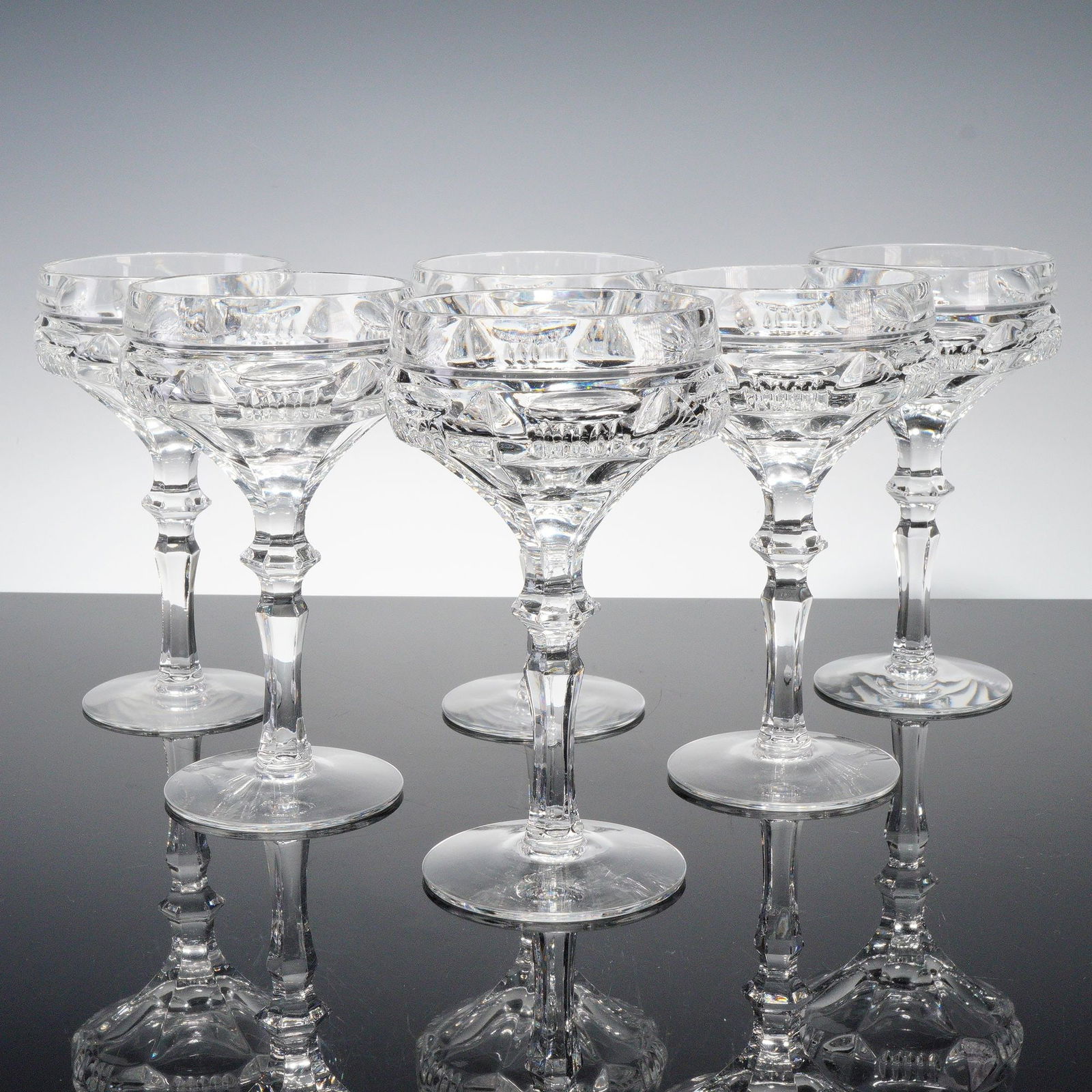 6pc Clear Cut Crystal Cocktail Coupes: Set of six clear cut crystal cocktail coupe glasses featuring faceted stems and geometric banding with fine prism detail. Elegant mid-century design, perfect for serving champagne or cocktails. Dimens