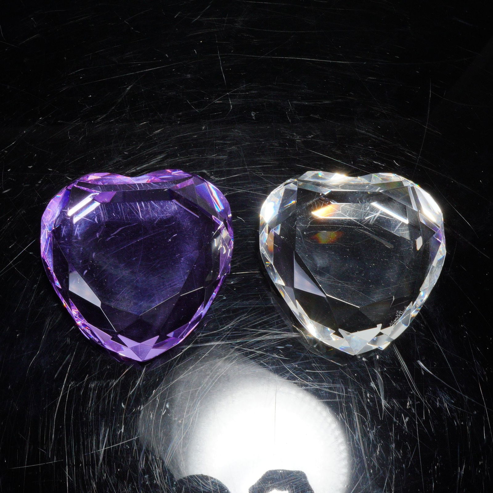 2pc Rosenthal Crystal Heart Paperweights: Two faceted crystal heart paperweights by Rosenthal. One in clear crystal and the other in purple coloration, each cut with multiple facets to reflect light from all angles. Both are etched with the R
