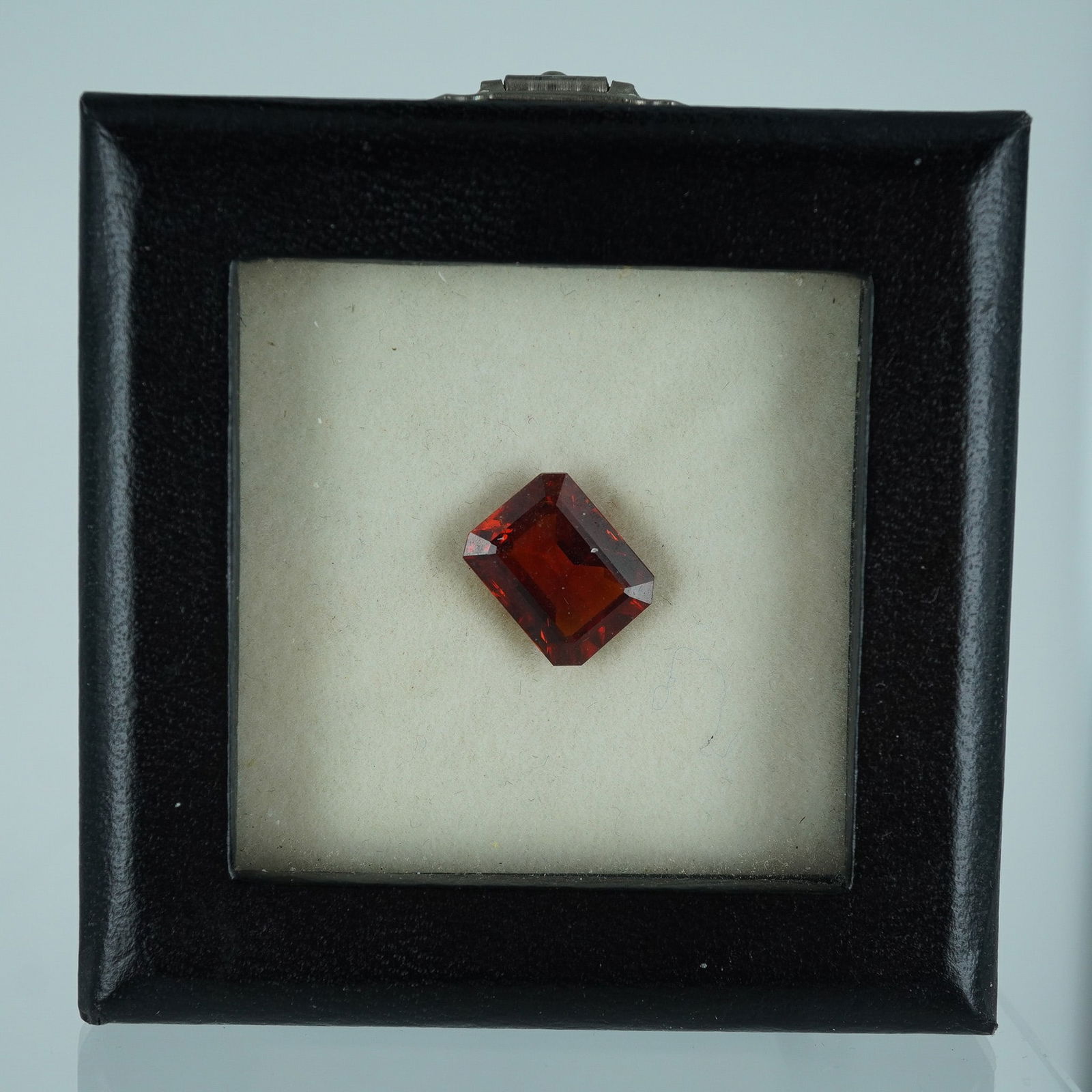 Deep Red Emerald Cut Gemstone: A faceted gemstone, likely a spessartite garnet, presented in a classic emerald cut. Exhibiting a rich deep red hue with excellent clarity and internal reflections, this gem is ideal for custom fine j