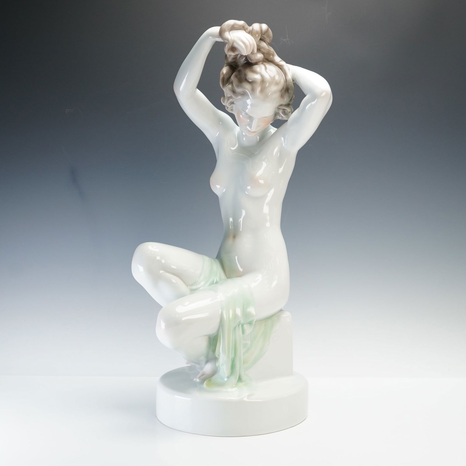 Herend by Elek Lux Porcelain Sculpture of Nude Maiden: Elegant porcelain sculpture designed by Elek Lux. The figure depicts a nude woman seated while arranging her hair, with a soft green drape accentuating the delicate form. Hand painted with a high glos