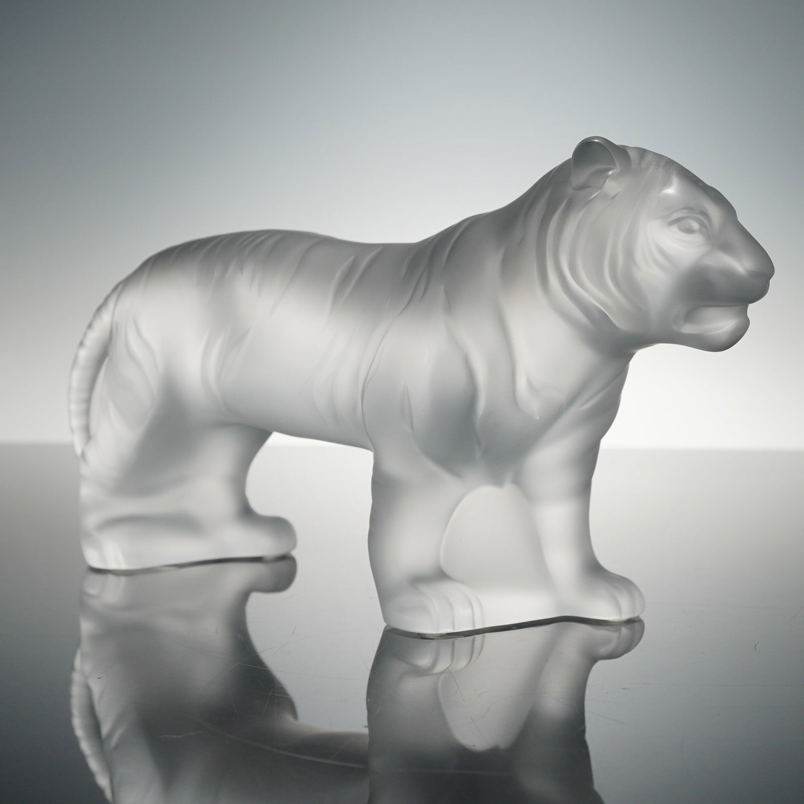 Lalique Frosted Crystal Figurine, Bengali Tiger: A finely crafted crystal sculpture depicting a majestic tiger rendered in satin-finished clear crystal. The piece showcases elegant fluidity and strength through detailed musculature and smooth contou