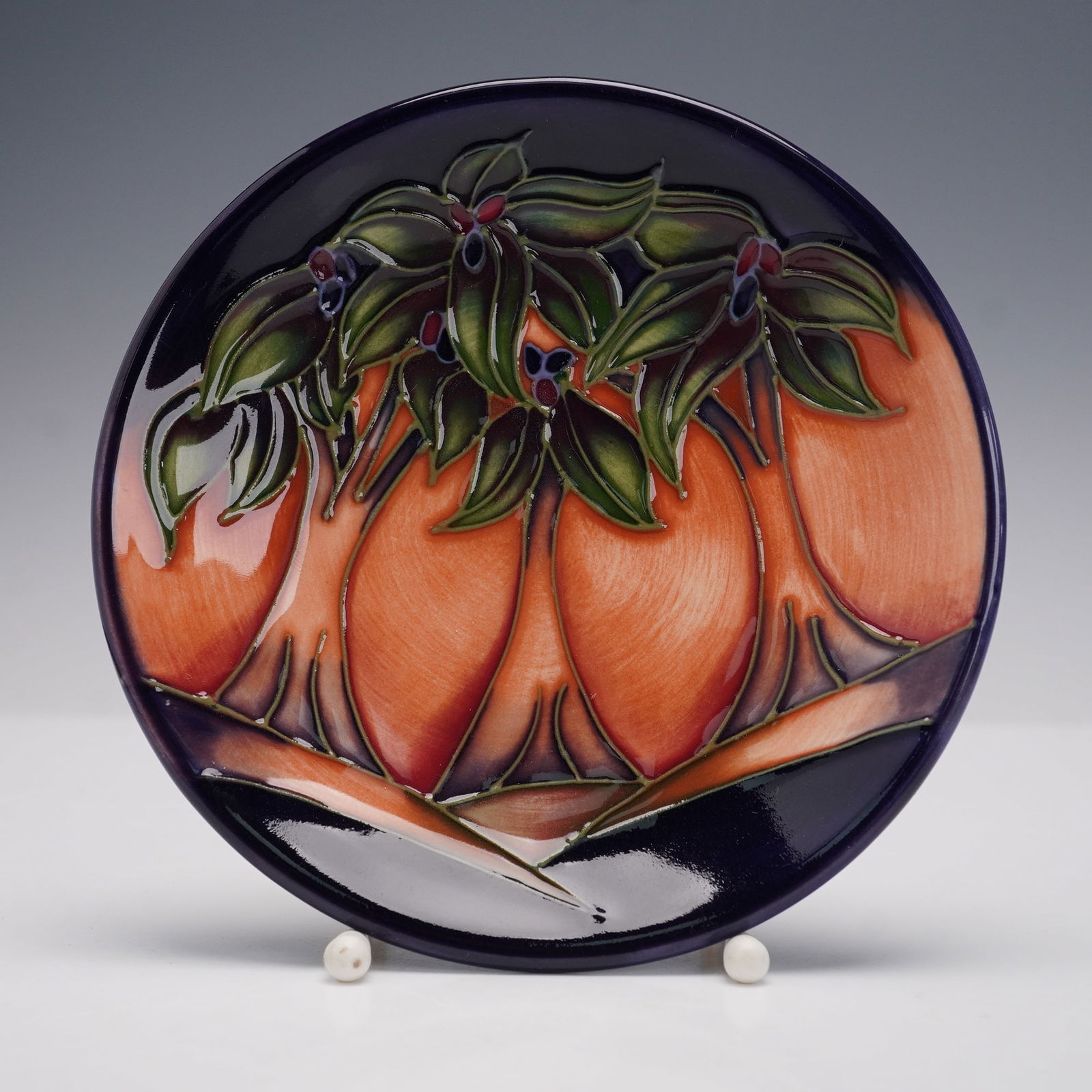 Moorcroft Pottery by Rachel Bishop Coaster Dish, New Forest: The circular ceramic dish features hand-decorated tubelined decoration with stylized orange fruit and green foliage against a deep cobalt ground. The underside is stamped Moorcroft and bears the Moorc