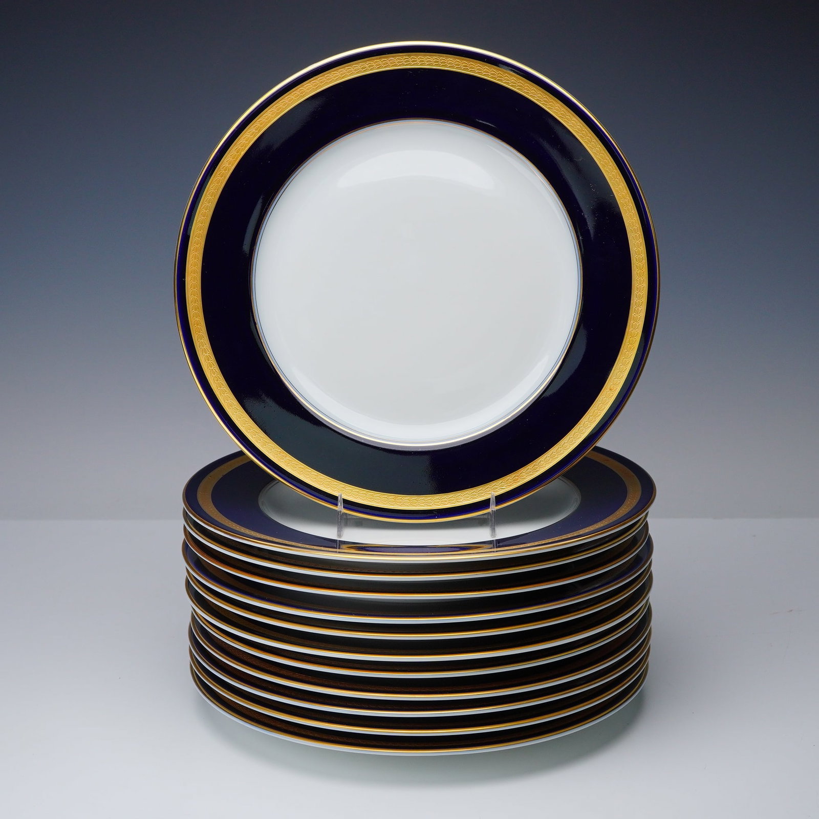 12pc Rosenthal Porcelain Dinner Plates, Eminence Cobalt Blue: A set of twelve Rosenthal porcelain dinner plates in the Eminence cobalt blue pattern, each featuring a wide deep blue border accented by an inner band of raised gilt decoration around a bright white