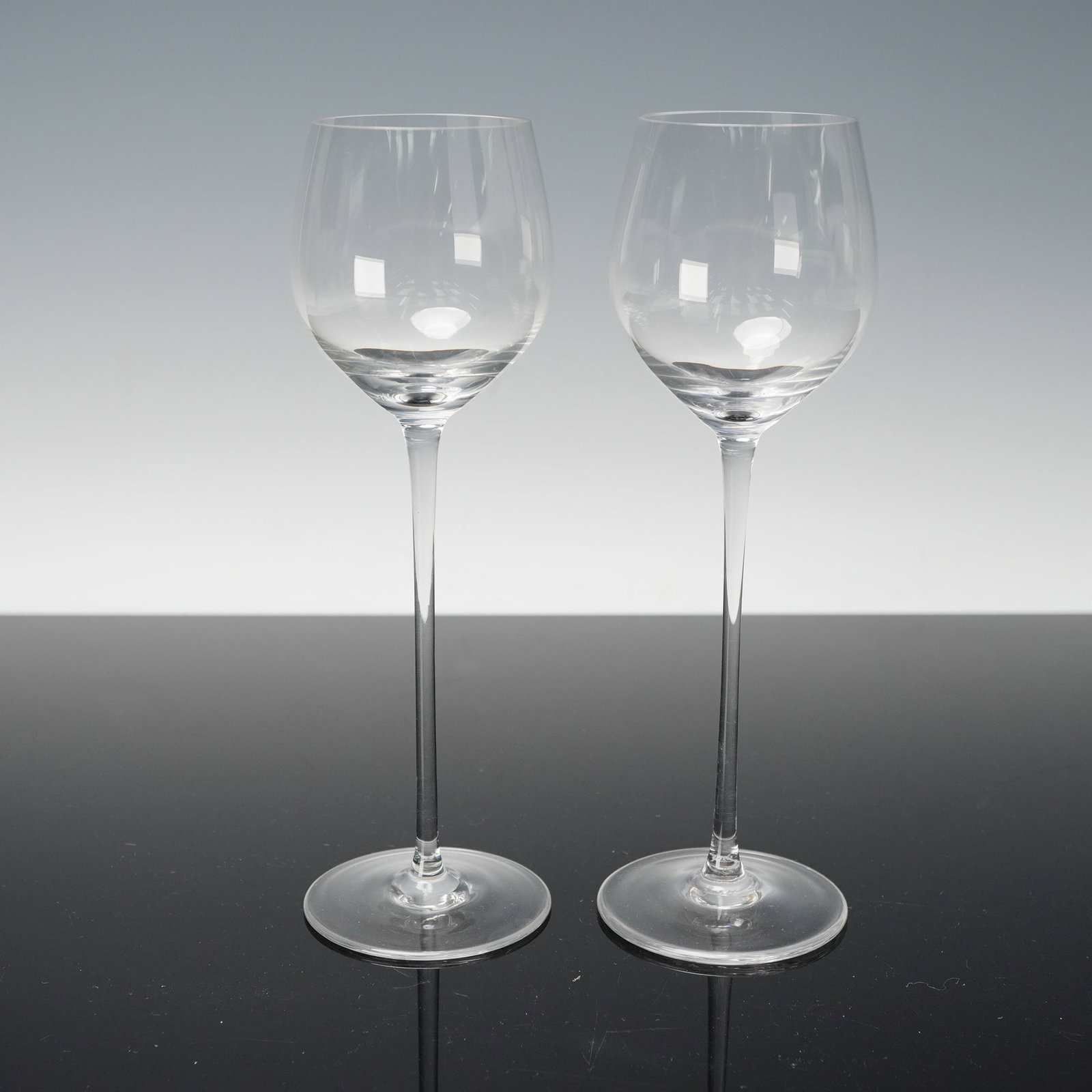 Pair of Riedel Crystal Sherry Glasses: A matching pair of clear Riedel crystal sherry glasses, each with a tall slender stem, rounded bowl, and circular foot, both pieces finely made in the classic Riedel style and each bearing the etched