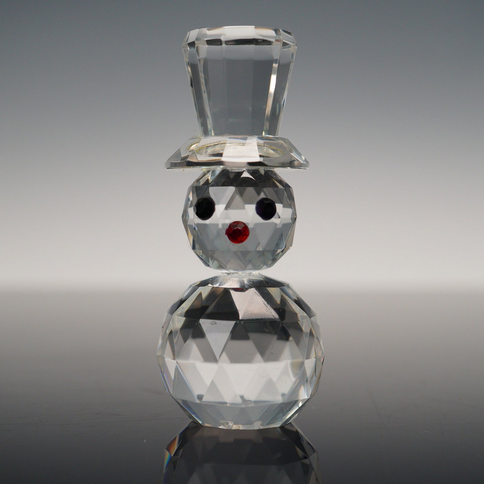 Cut Glass Snowman Figurine: A delightful cut glass snowman figurine with finely faceted crystal that shimmers in the light. The figure features two stacked spheres, a tall faceted hat, and a cheerful face accented with black cry