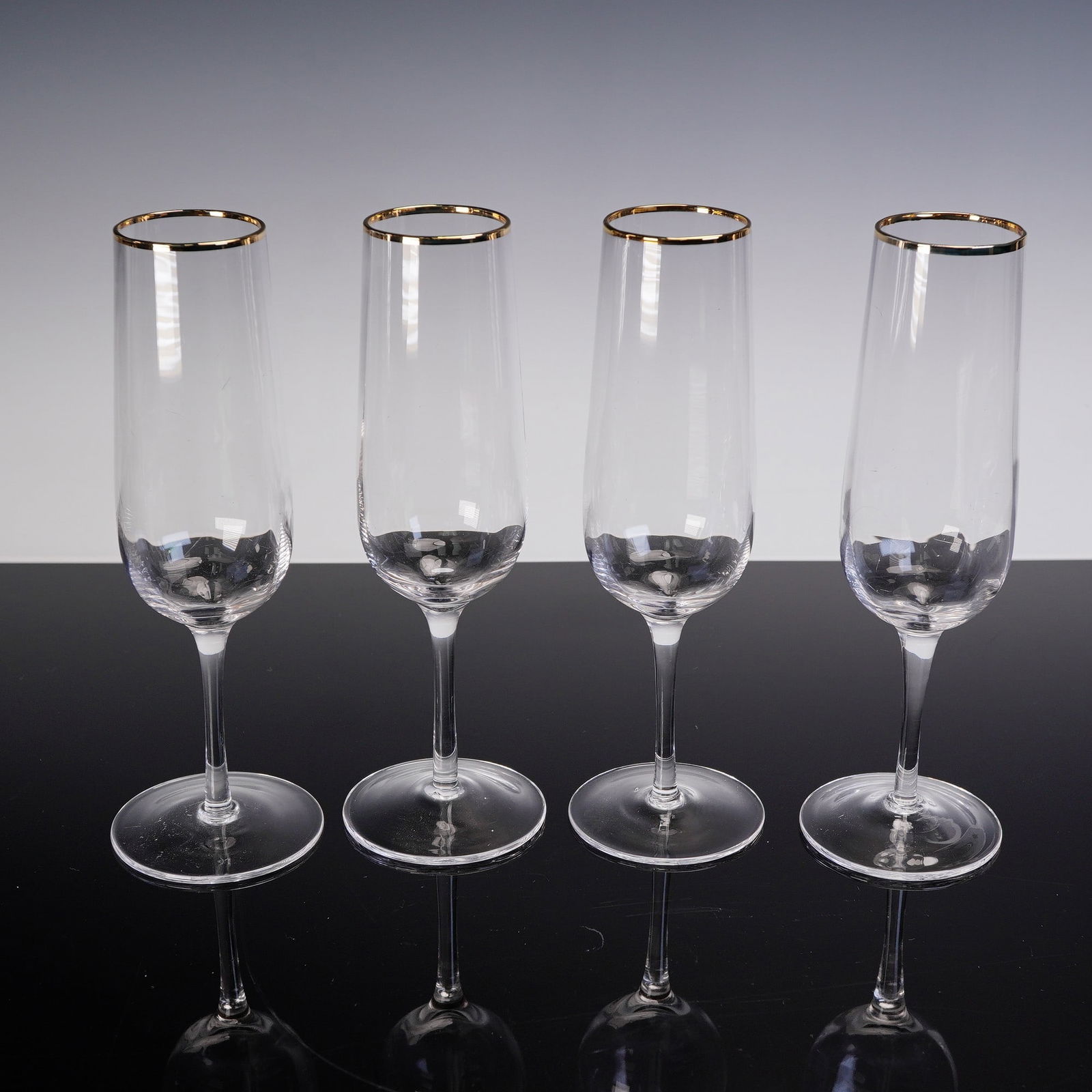 4pc Martha Stewart Champagne Glass Set with Gold Rim: Set of four clear glass champagne flutes, each featuring a slender stem and elongated bowl. The glasses are accented with a gold band around the rim. Dimensions: 3"W x 9"H Country of Origin: United St