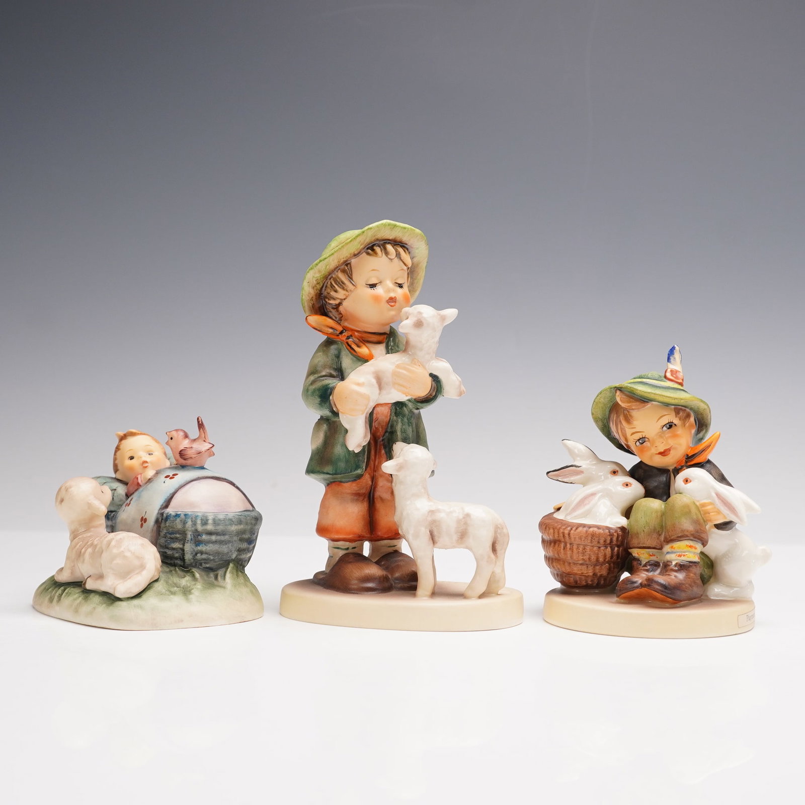 3pc Goebel Hummel Animal Companion Figurines: Three animal companion porcelain figurines including The Guardian (214) depicting a child resting with a lamb and birds, Shepherds Boy (64) showing a young boy holding and tending to lambs, and Playma