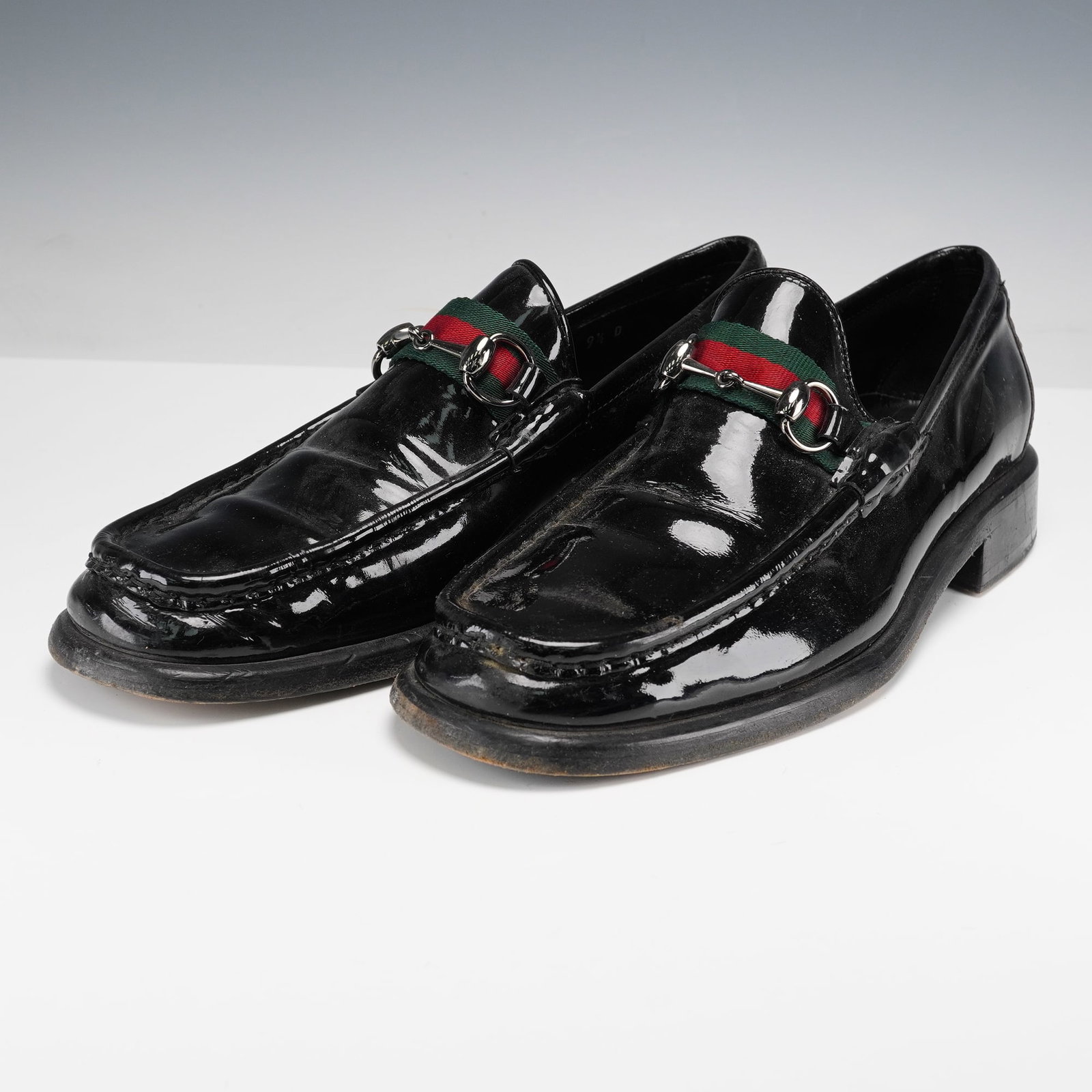 Gucci Men's Black Patent Leather Loafers with Web Strap: These Gucci men's black patent leather loafers feature the brand's iconic green and red web strap detail with silver-tone hardware across the vamp. The sleek design is perfect for both casual and semi