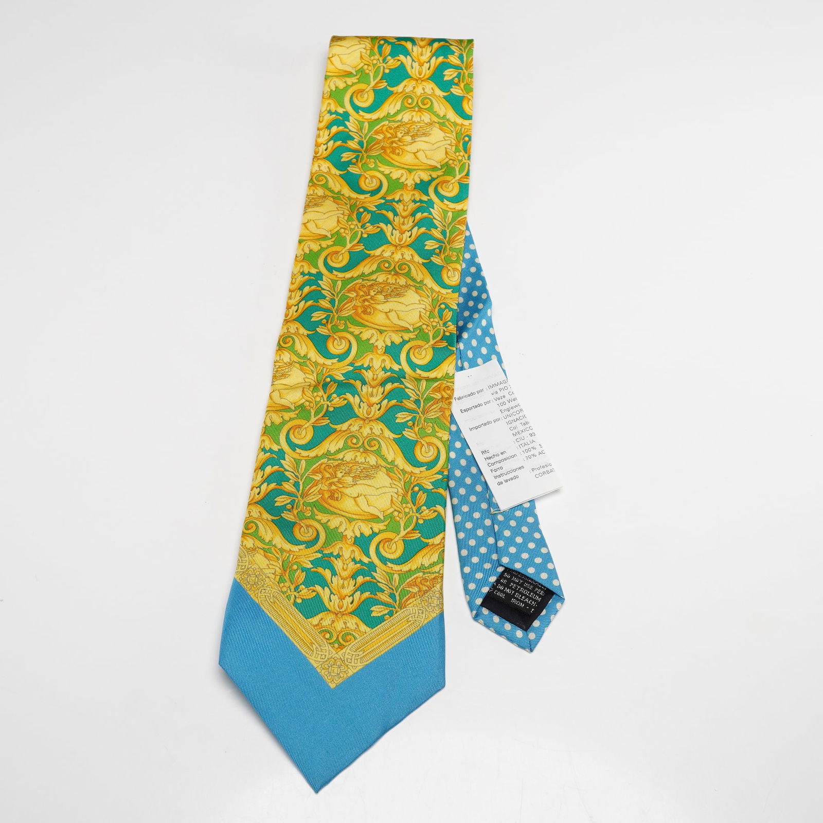 V2 by Versace Silk Necktie Baroque Pattern: V2 by Versace pure silk necktie featuring a vivid baroque inspired pattern in gold and turquoise with ornate scrolling motifs, accented by a contrasting light blue polka dot section on the underside a