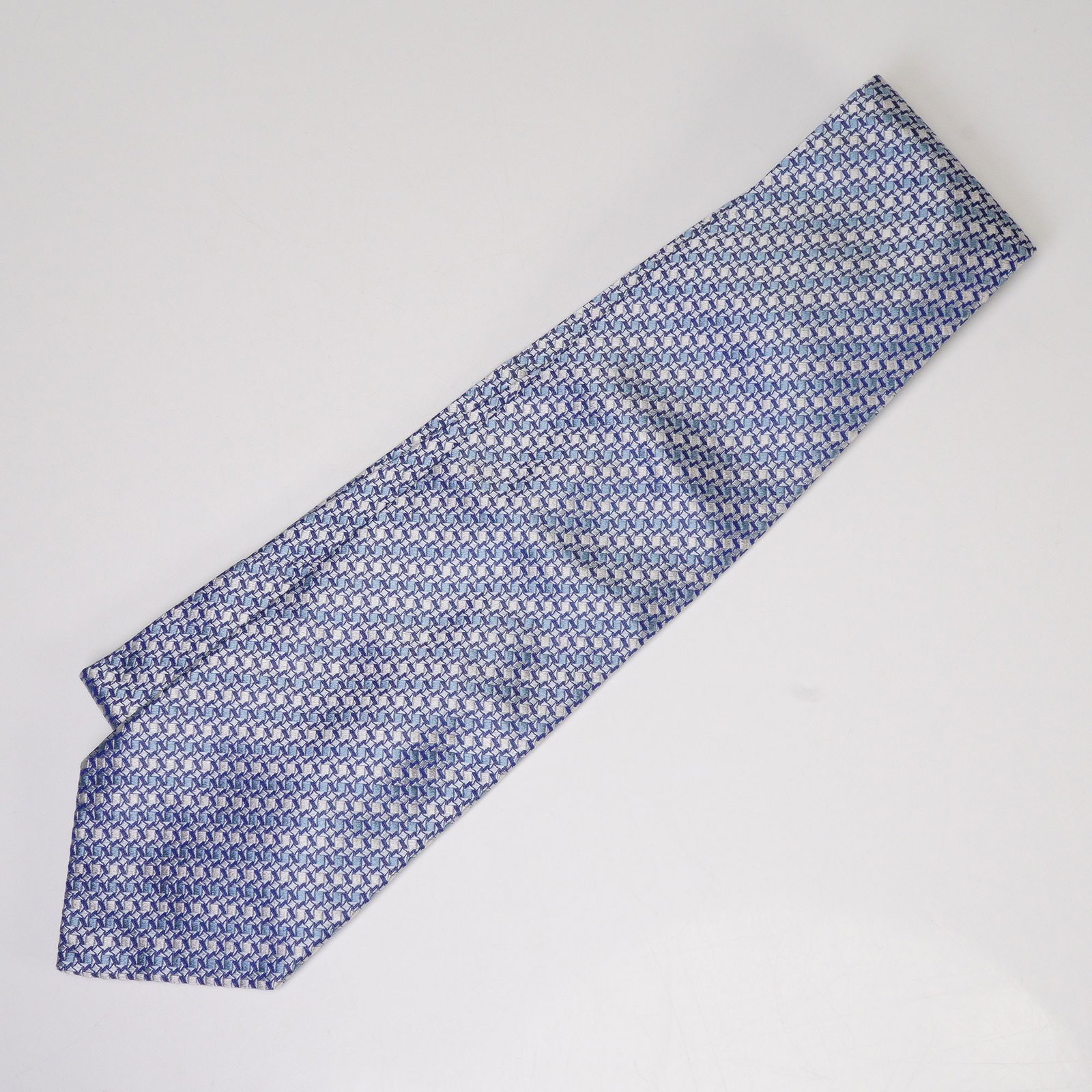 Escada Blue Geometric Silk Tie: An Escada 100% silk tie featuring an intricate geometric pattern in shades of blue and silver. Finely crafted in Italy, this elegant accessory showcases the brand's attention to detail and luxurious f