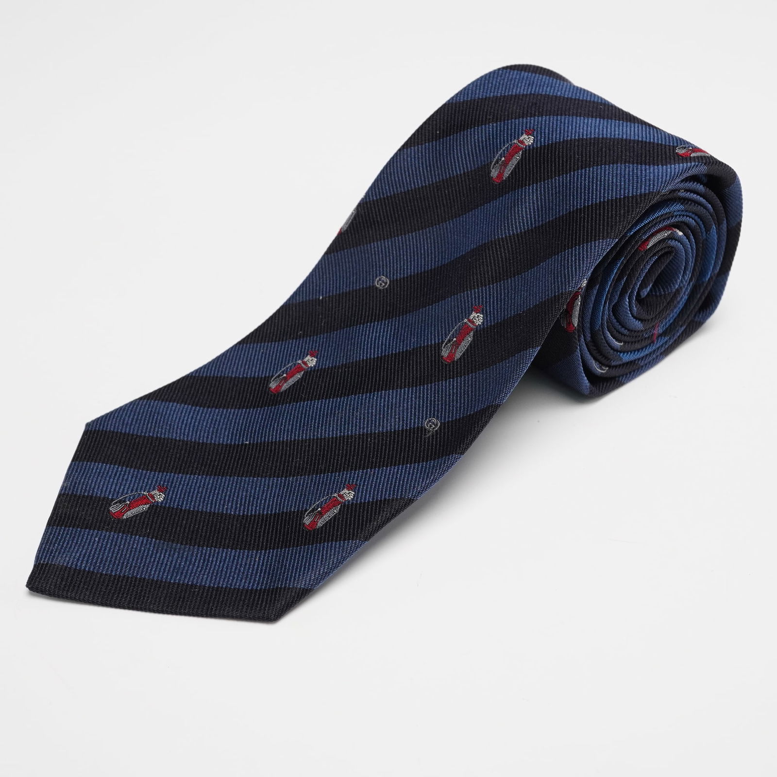 Gucci Silk Necktie, Blue Striped Golf Bag Pattern: Gucci pure silk necktie featuring diagonal navy and blue stripes decorated with finely embroidered golf bags and subtle interlocking G accents woven into the design. Dimensions: 54"L x 3.5"W Country o
